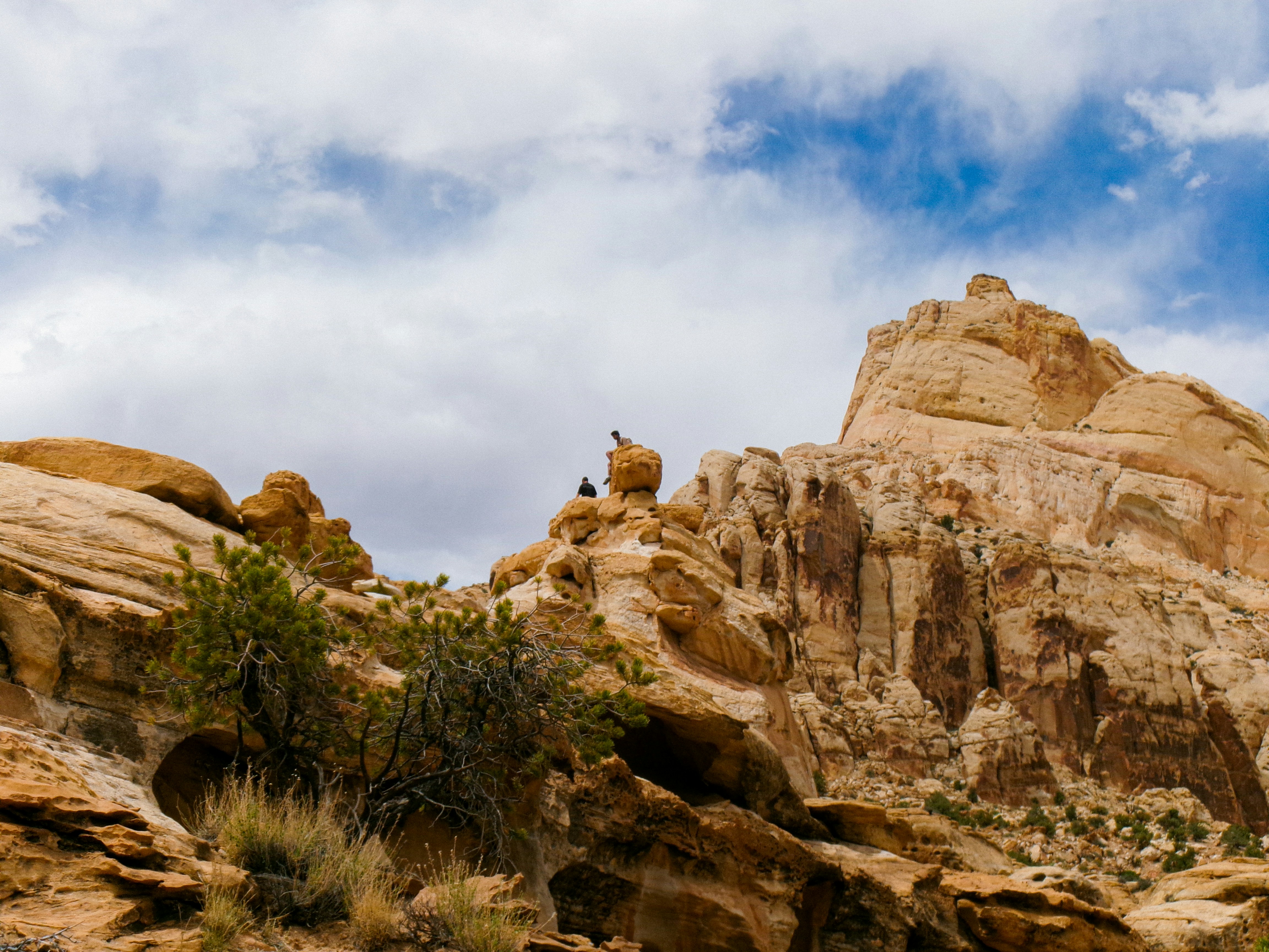 Two figures on desert rock formations under a cloudy sky