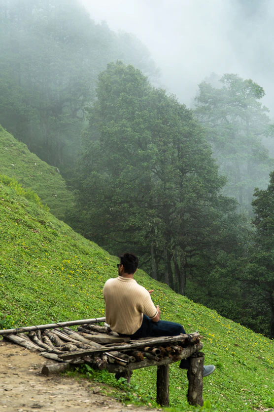 Man on bench watches foggy green mountain scenery