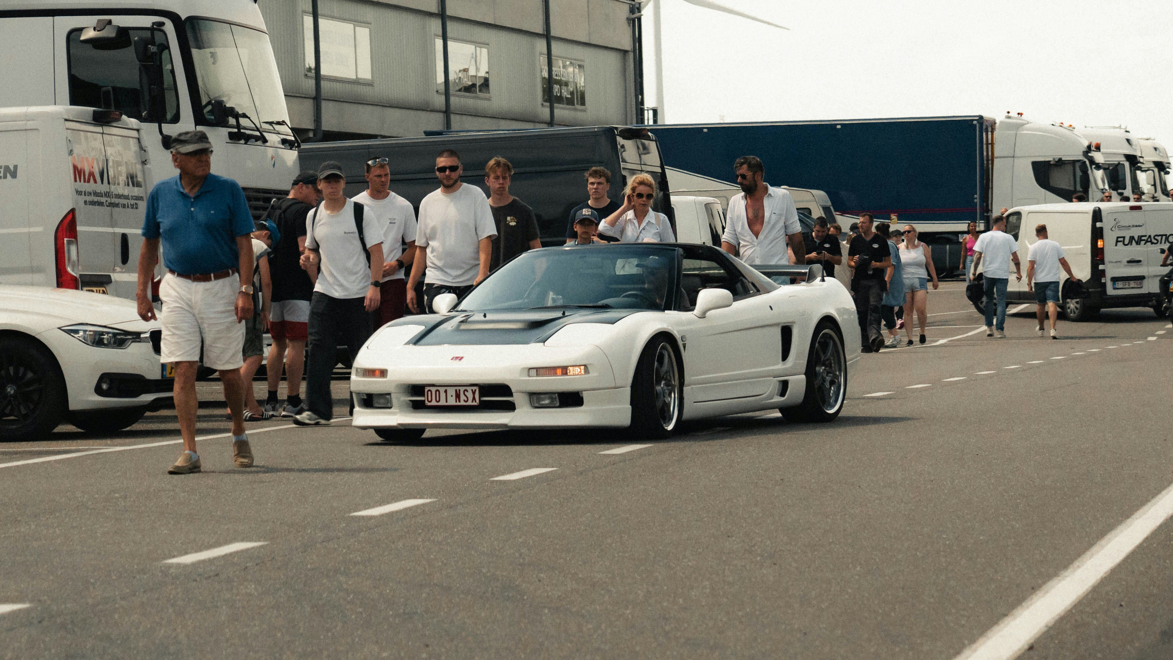 Voiture de sport blanche sur la piste avec des spectateurs et des camions.