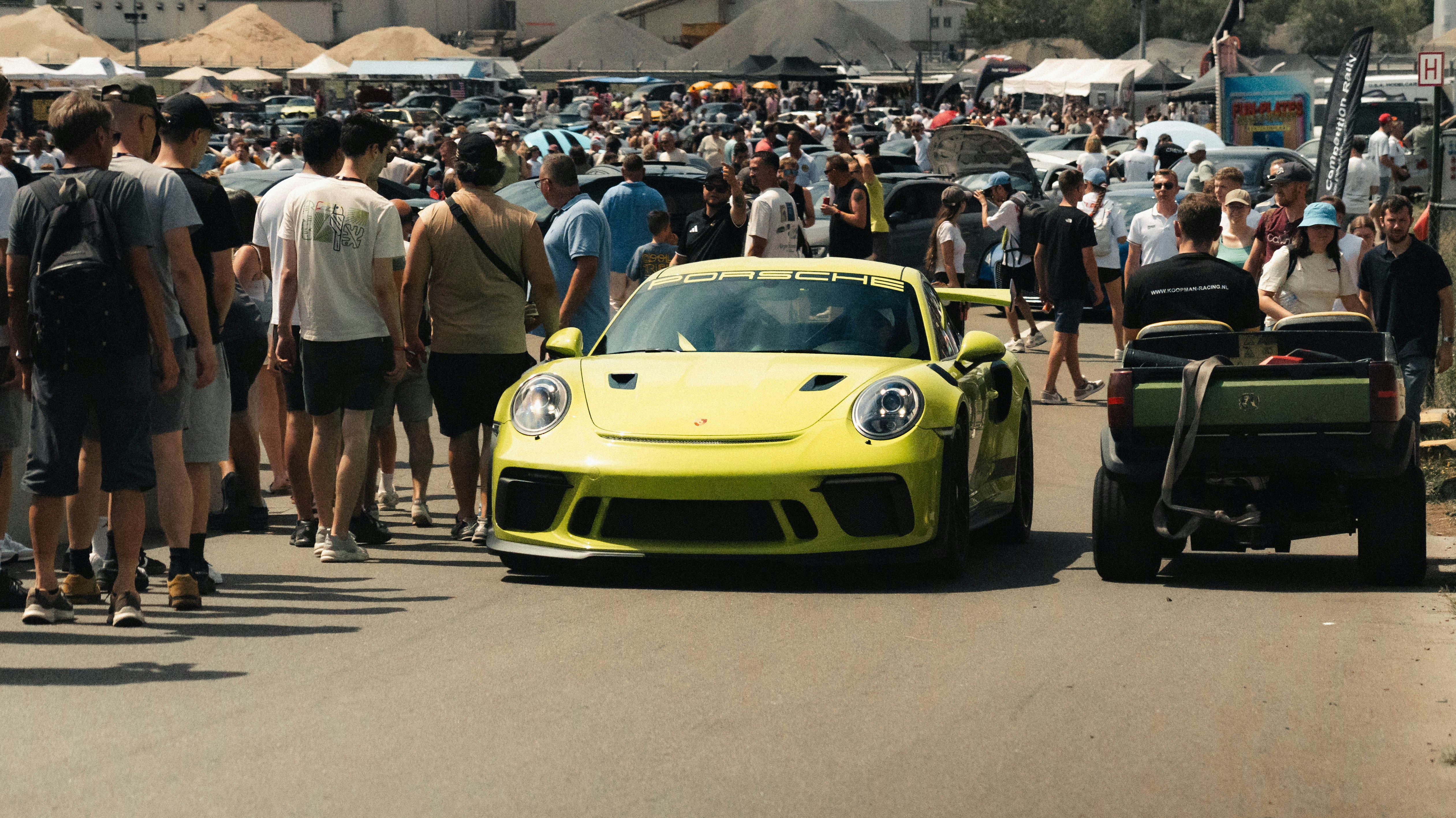 Voiture de sport Porsche jaune traversant une grande foule.