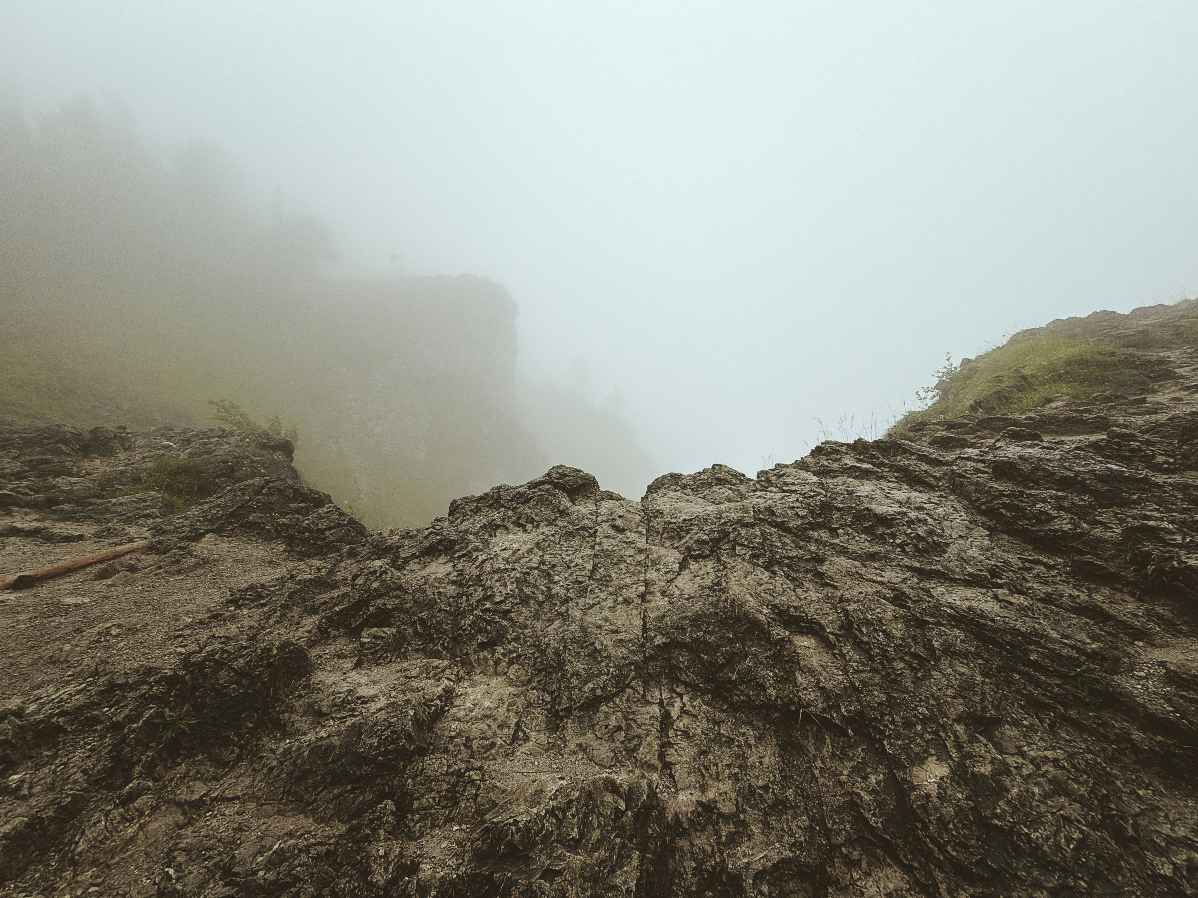 Rocky cliff edge overlooking a foggy, misty landscape.