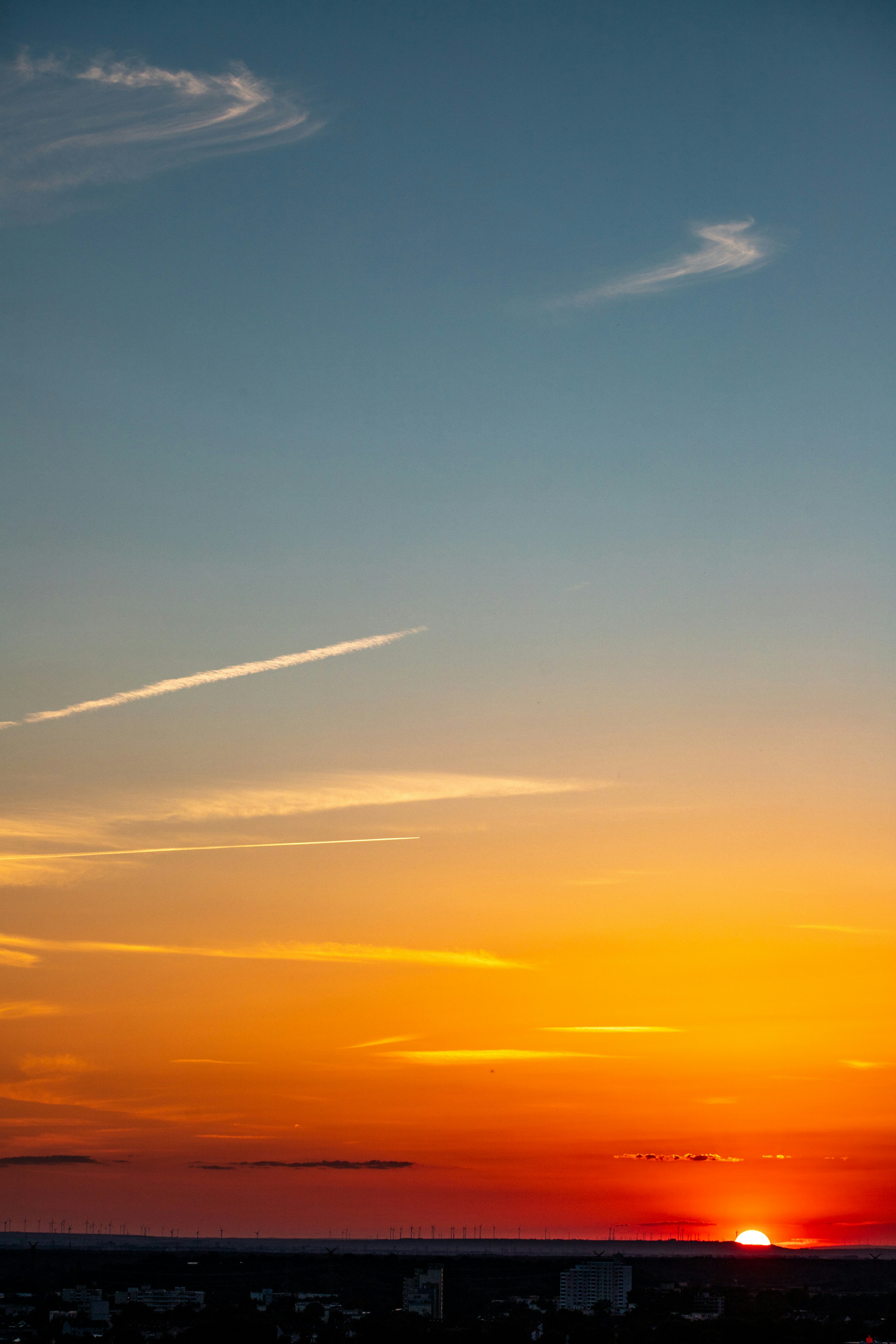 Vibrant sunset sky over a city skyline with contrails.