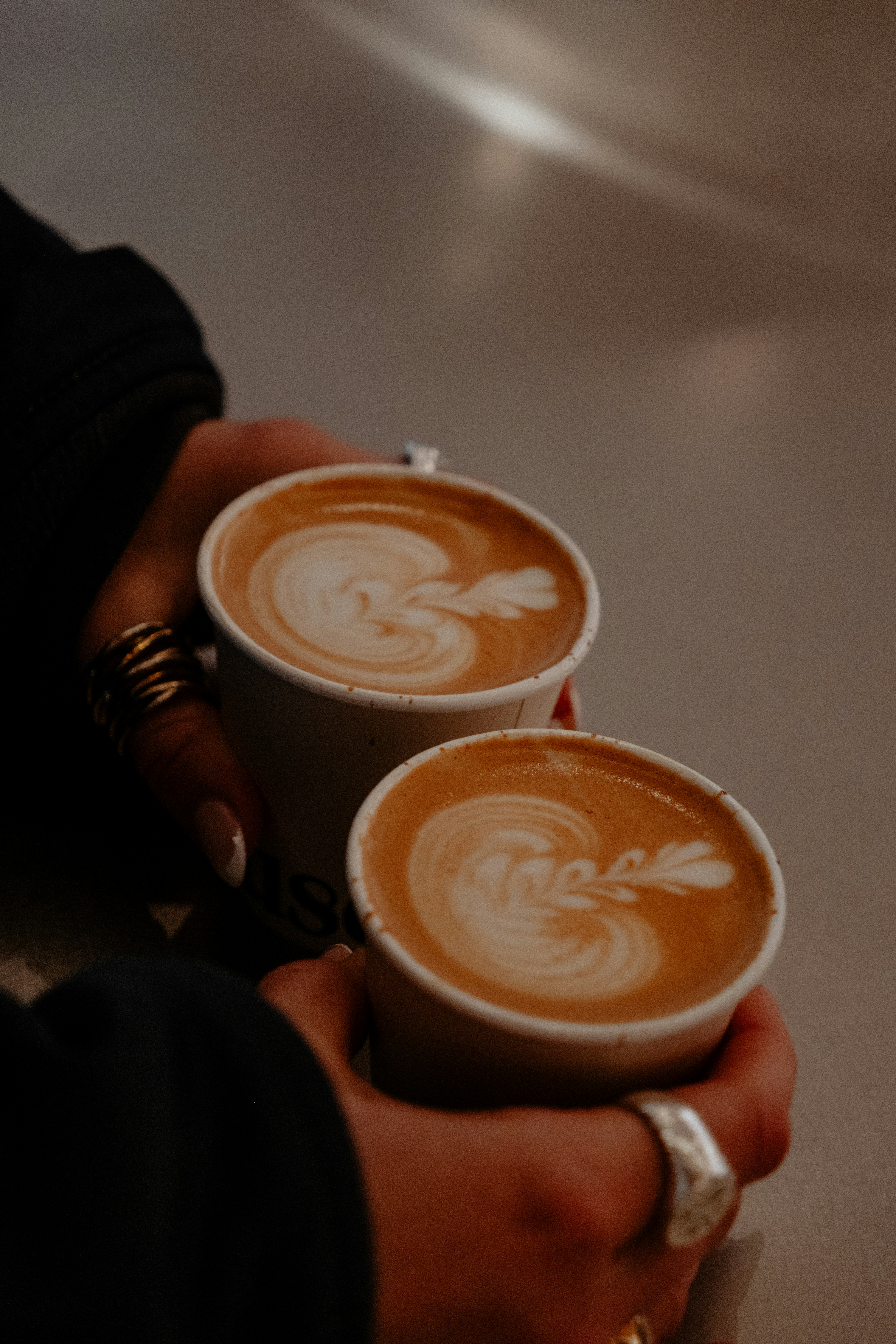 Two hands holding two cups of coffee with latte art.