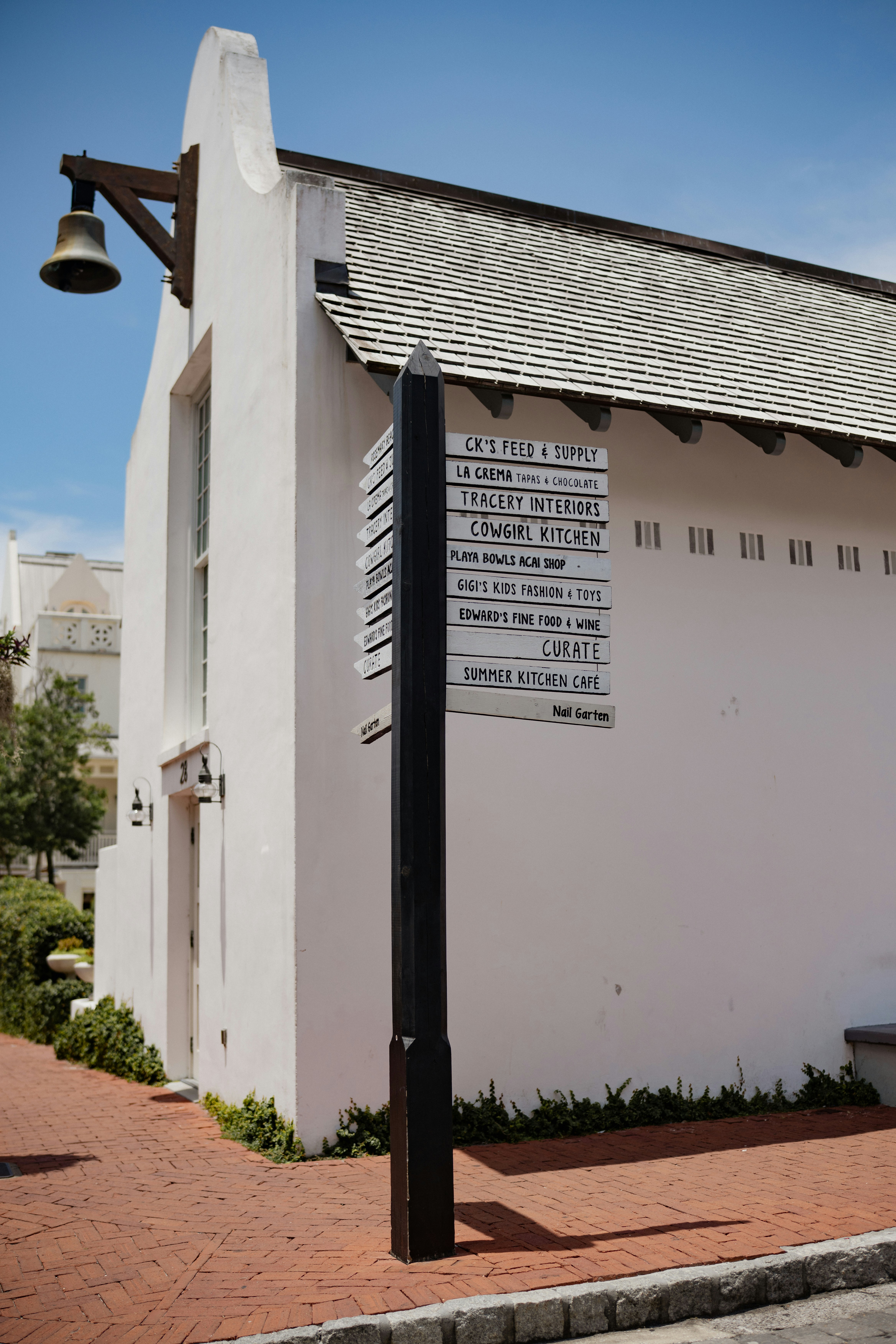 A white building with a bell and a multi-directional signpost.