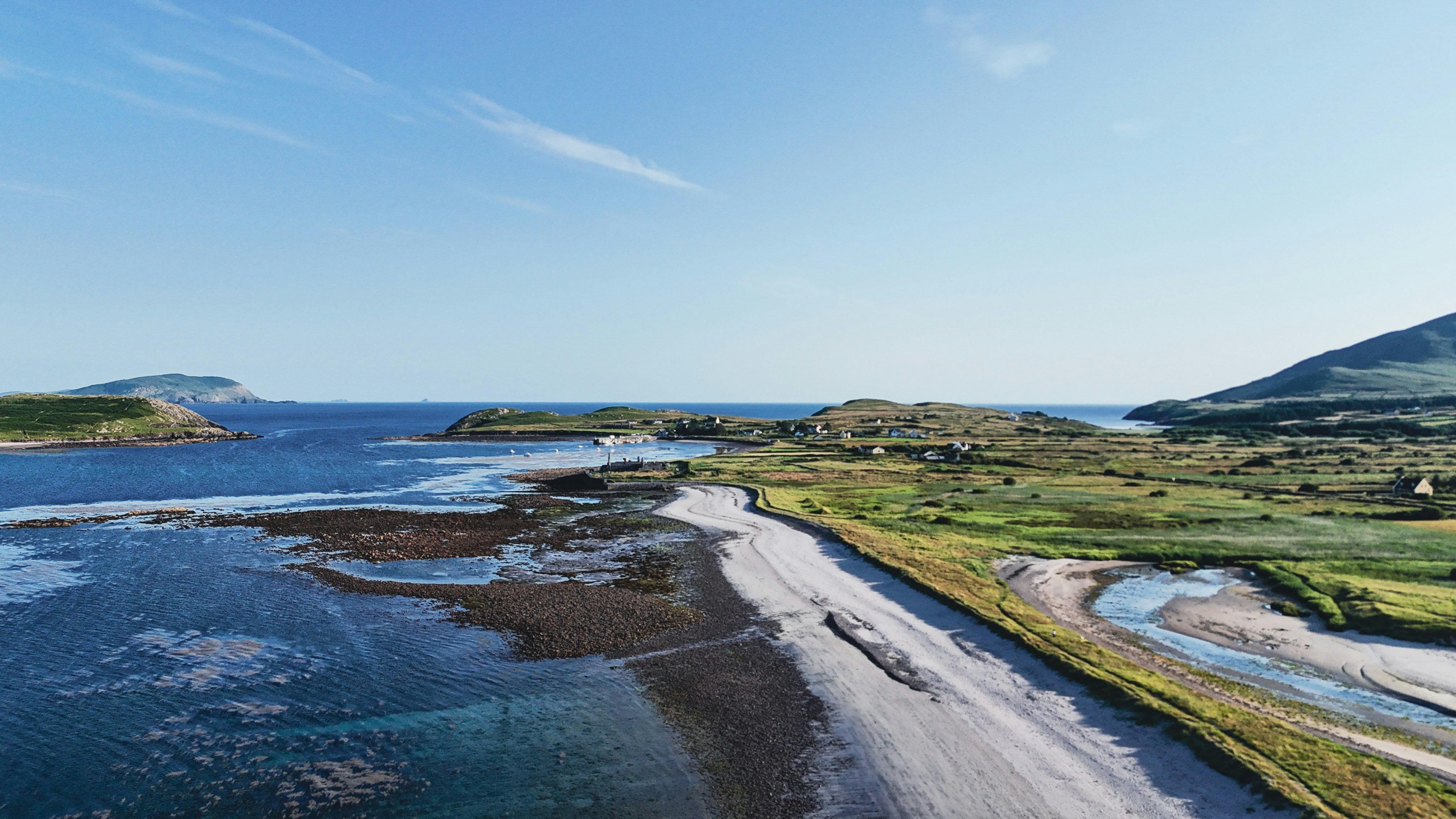 Aerial view of a sandy beach, ocean, and green coastline.