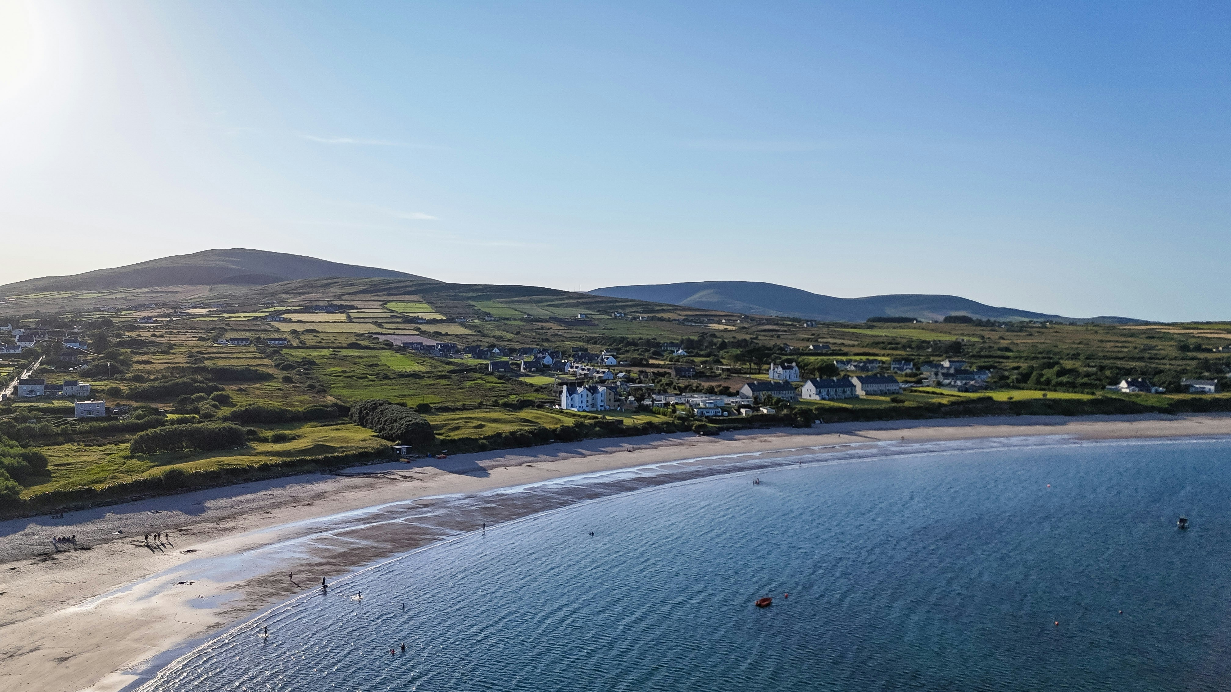 Aerial view of a sunny beach, village, and green hills.