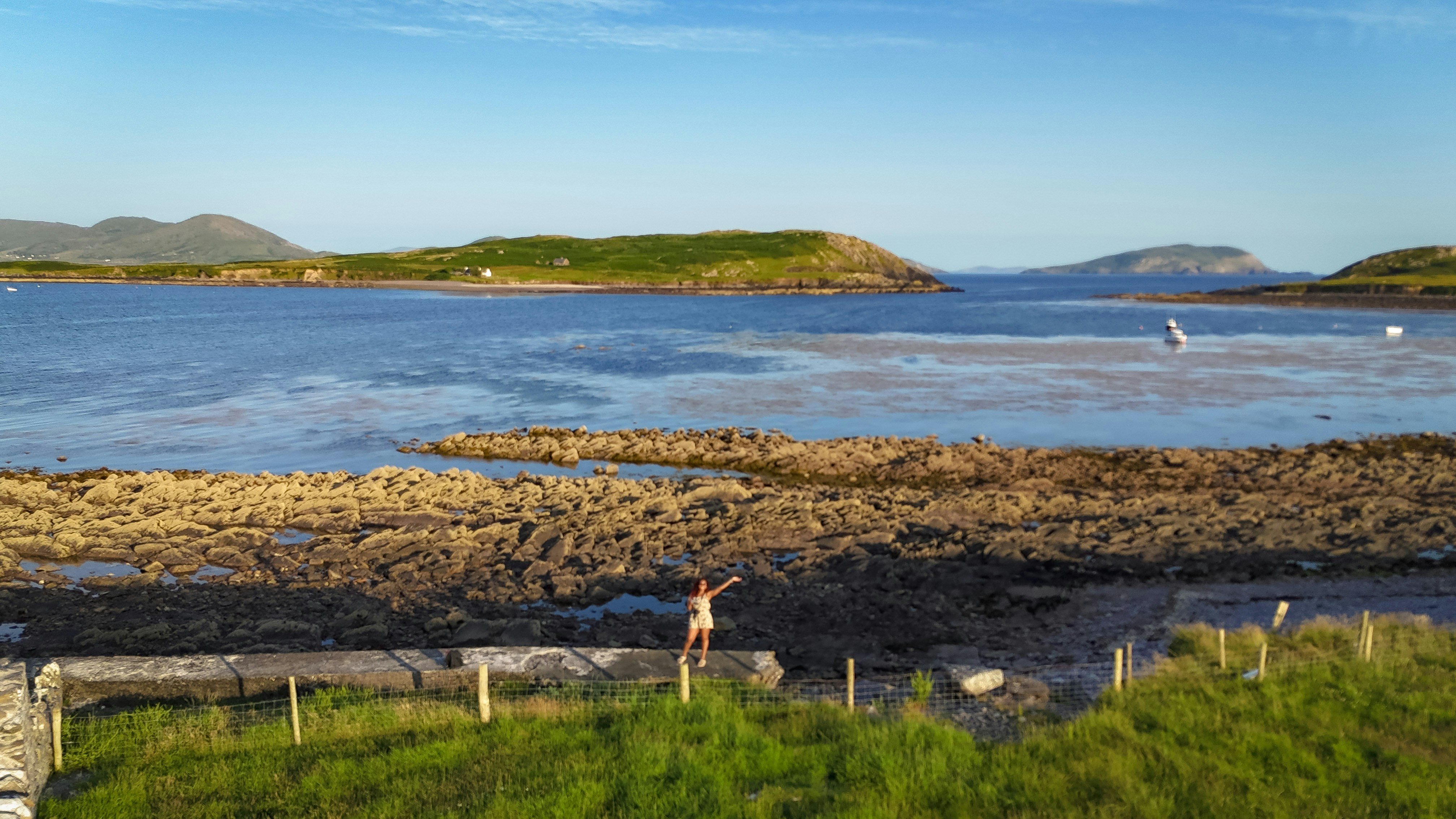 A person balancing on a wall by a coastal bay.
