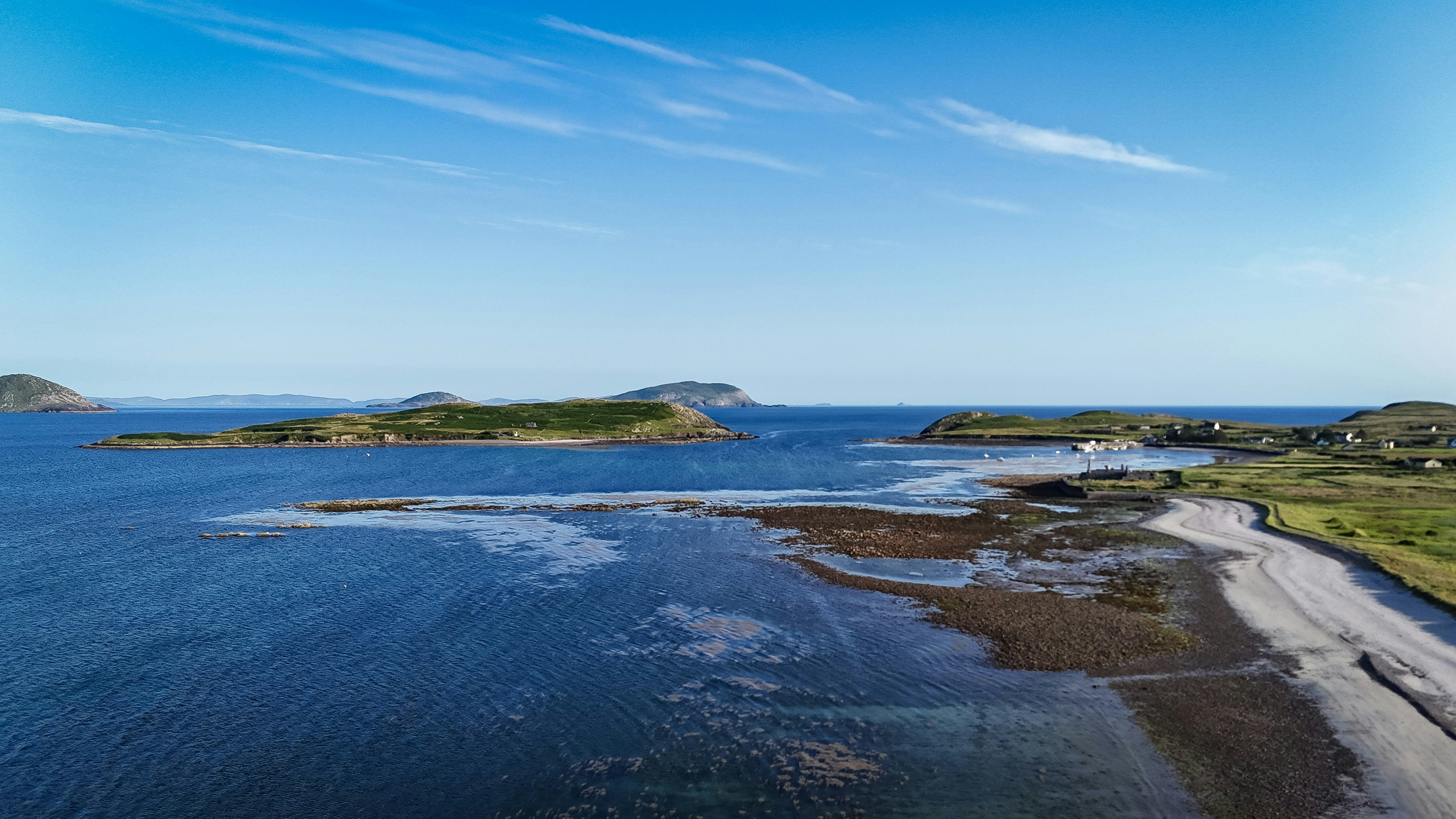 Islands and ocean meet a clear sky and coastal shore.