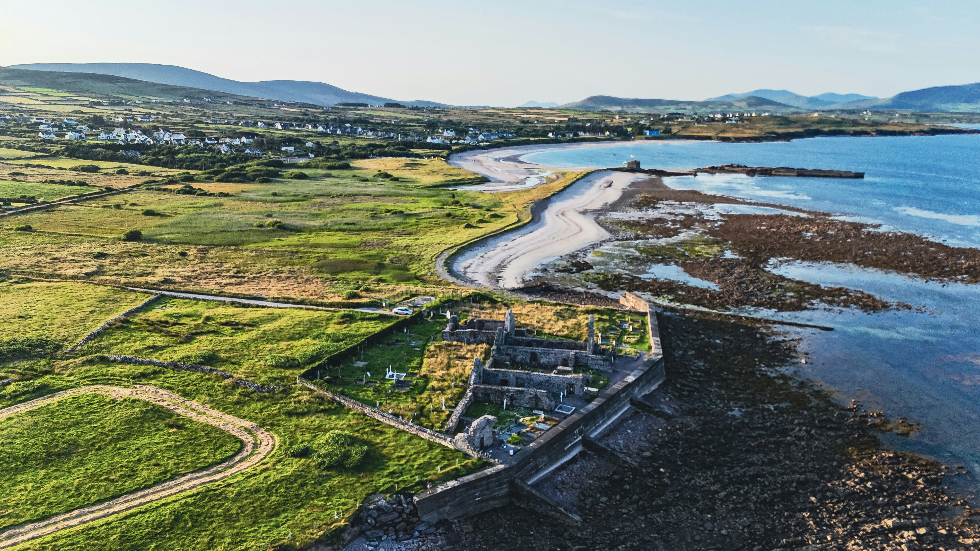 Aerial view of coastal ruins, beach, and a distant town.