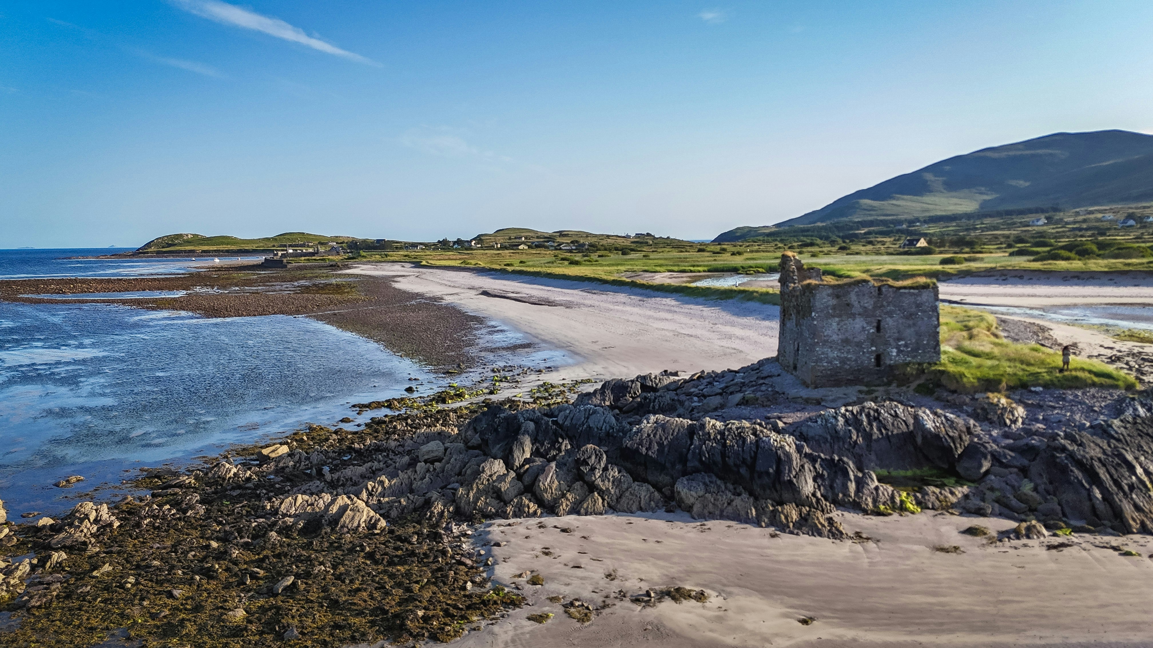 Old stone building on a rocky beach with mountains.