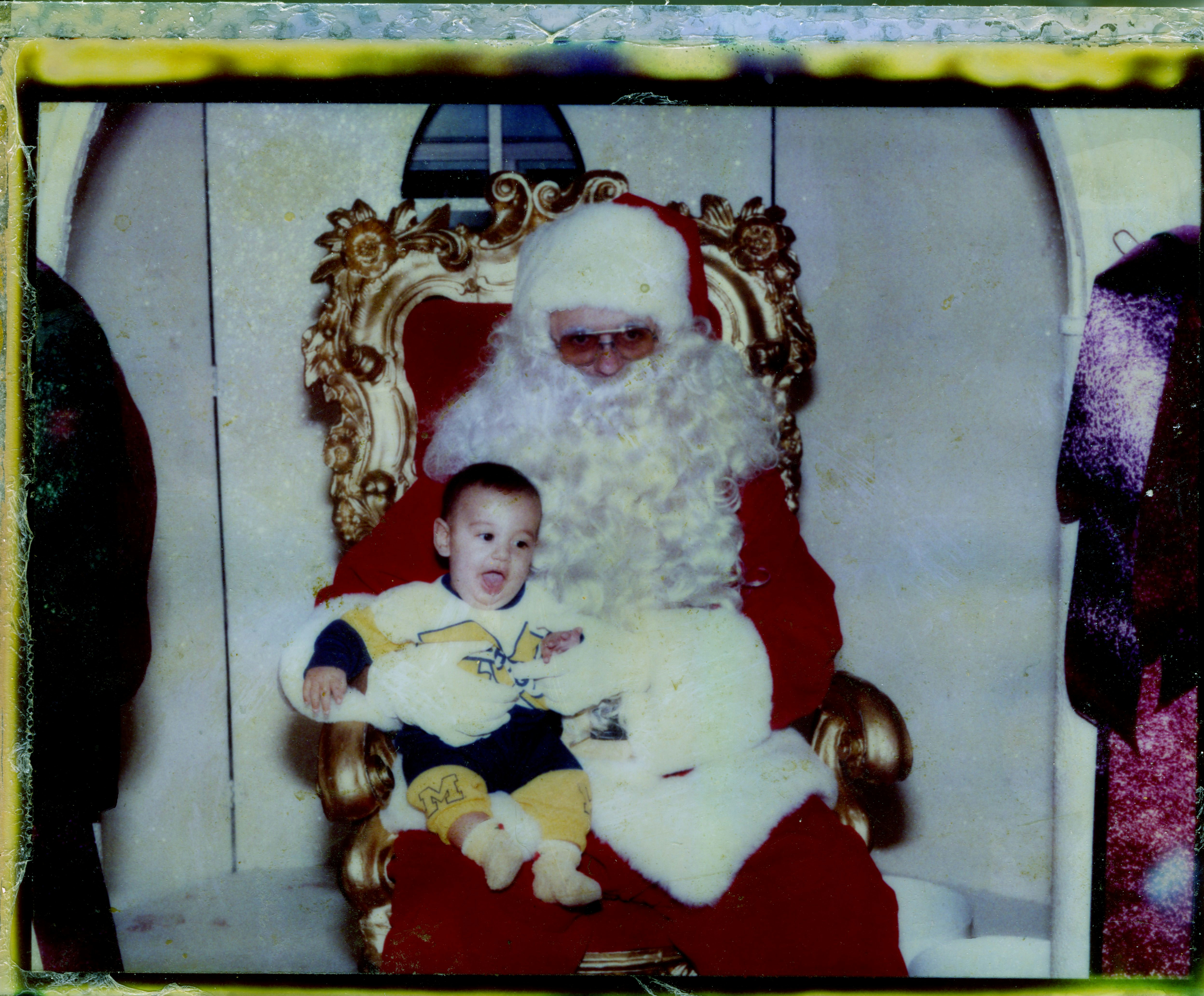 A baby smiles while sitting on santa claus's lap.