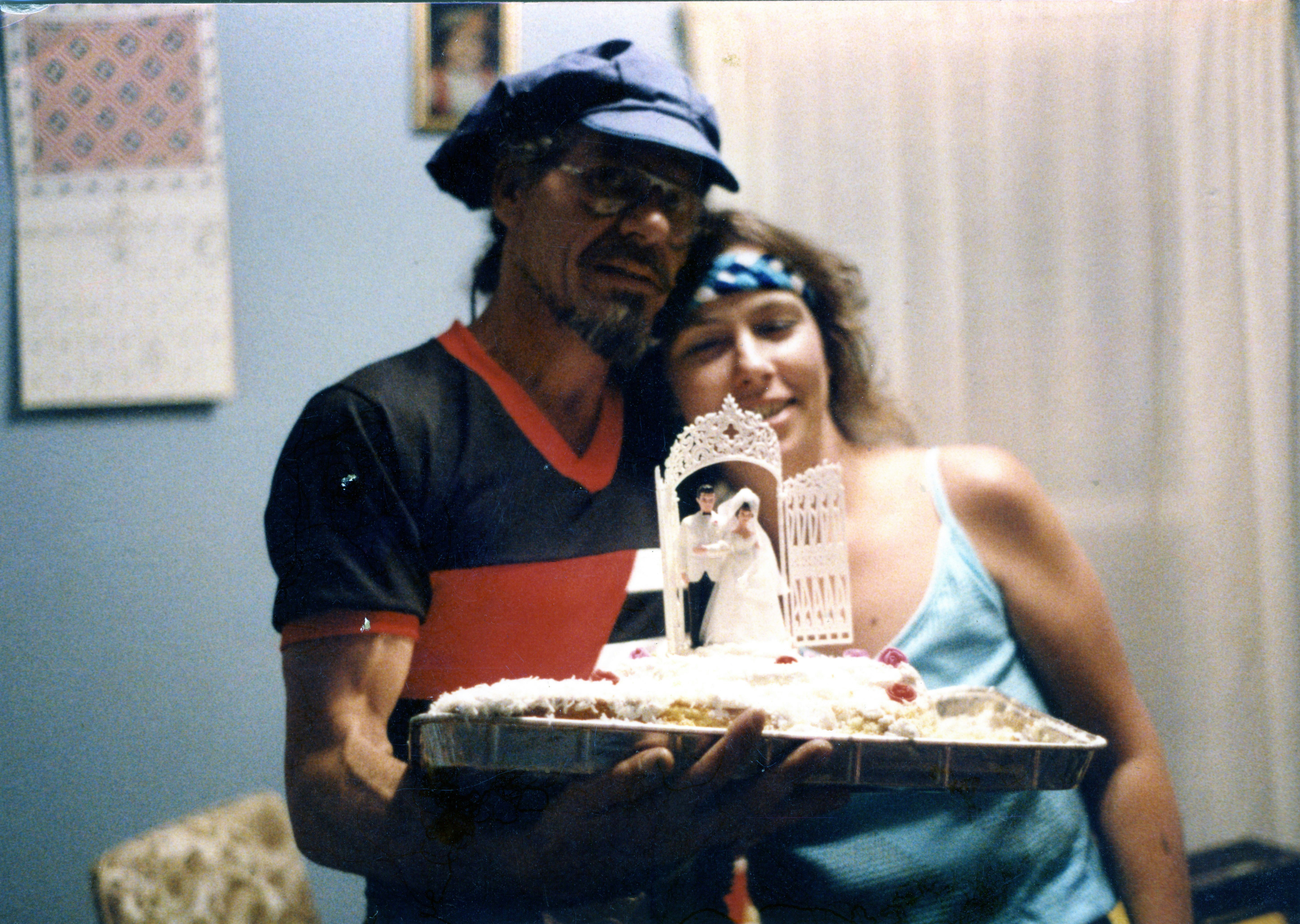 Man and woman holding a cake with a wedding topper.