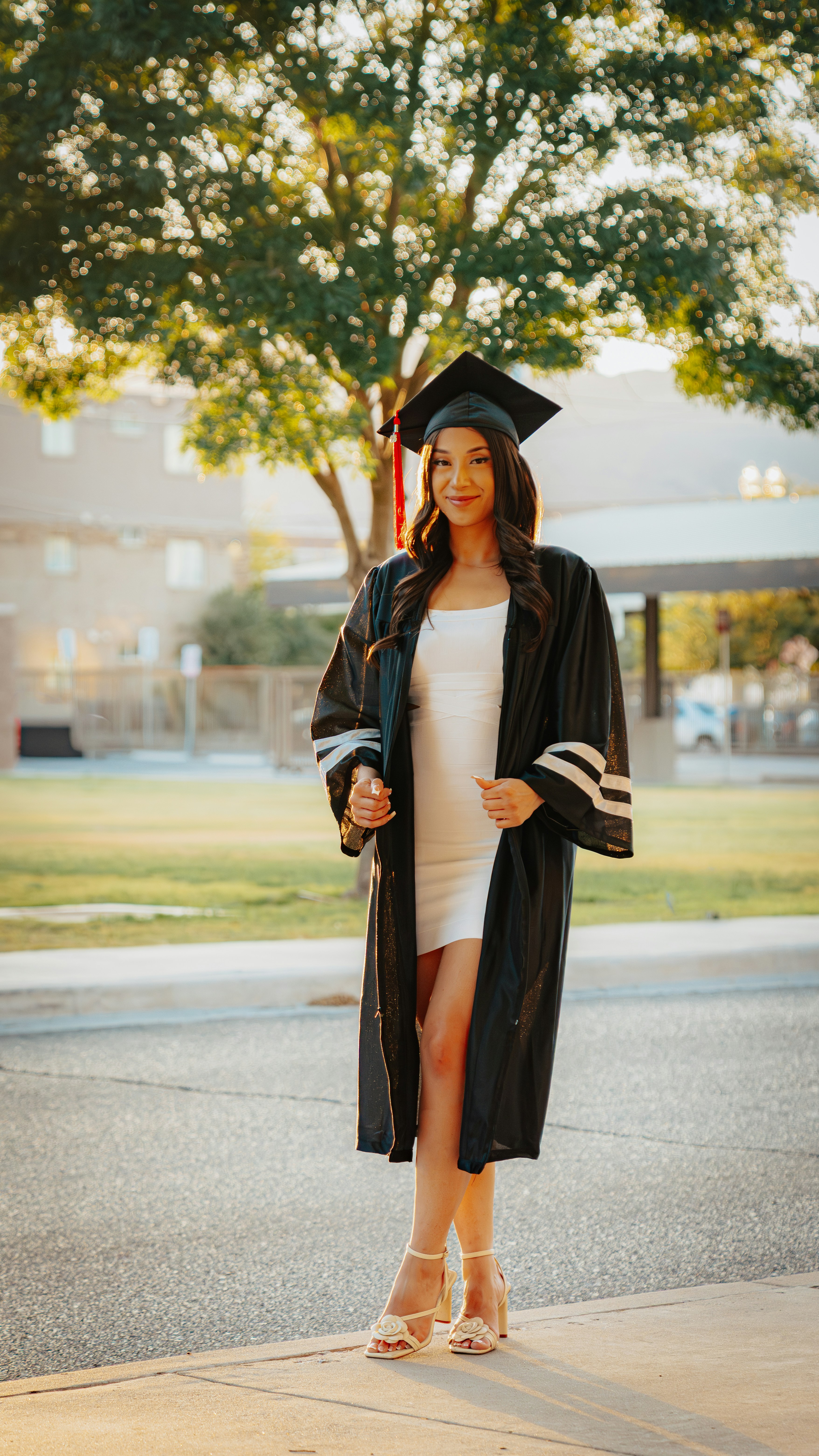 A young woman in a graduation gown and cap outdoors.
