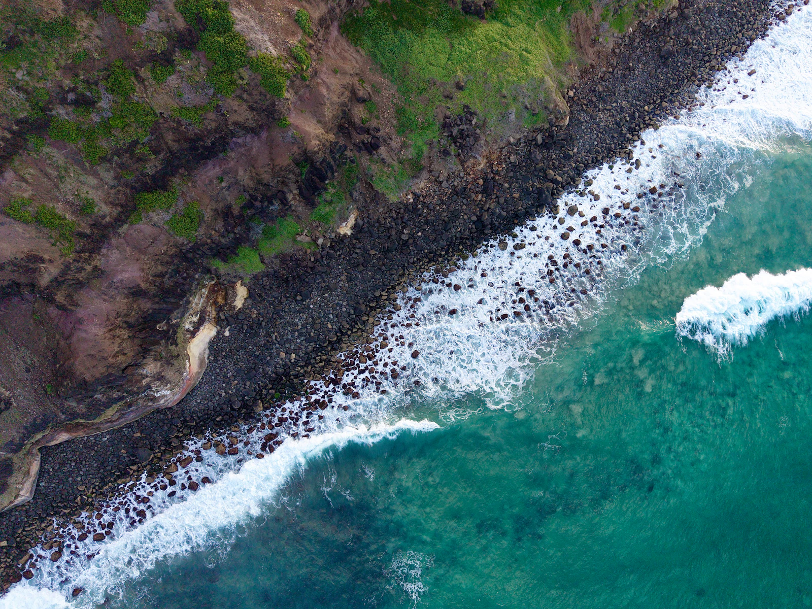 Green coastal cliffs meeting turquoise surf at Lennox Head, near Camp Drewe