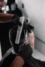 A barber in black gloves cutting a man's hair.