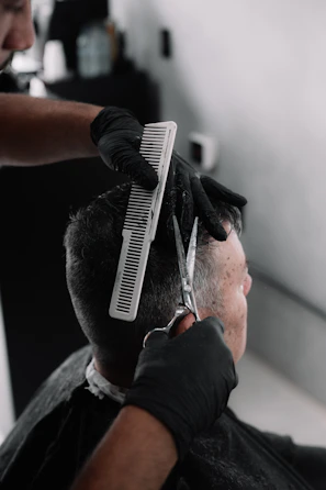 A barber in black gloves cutting a man's hair.