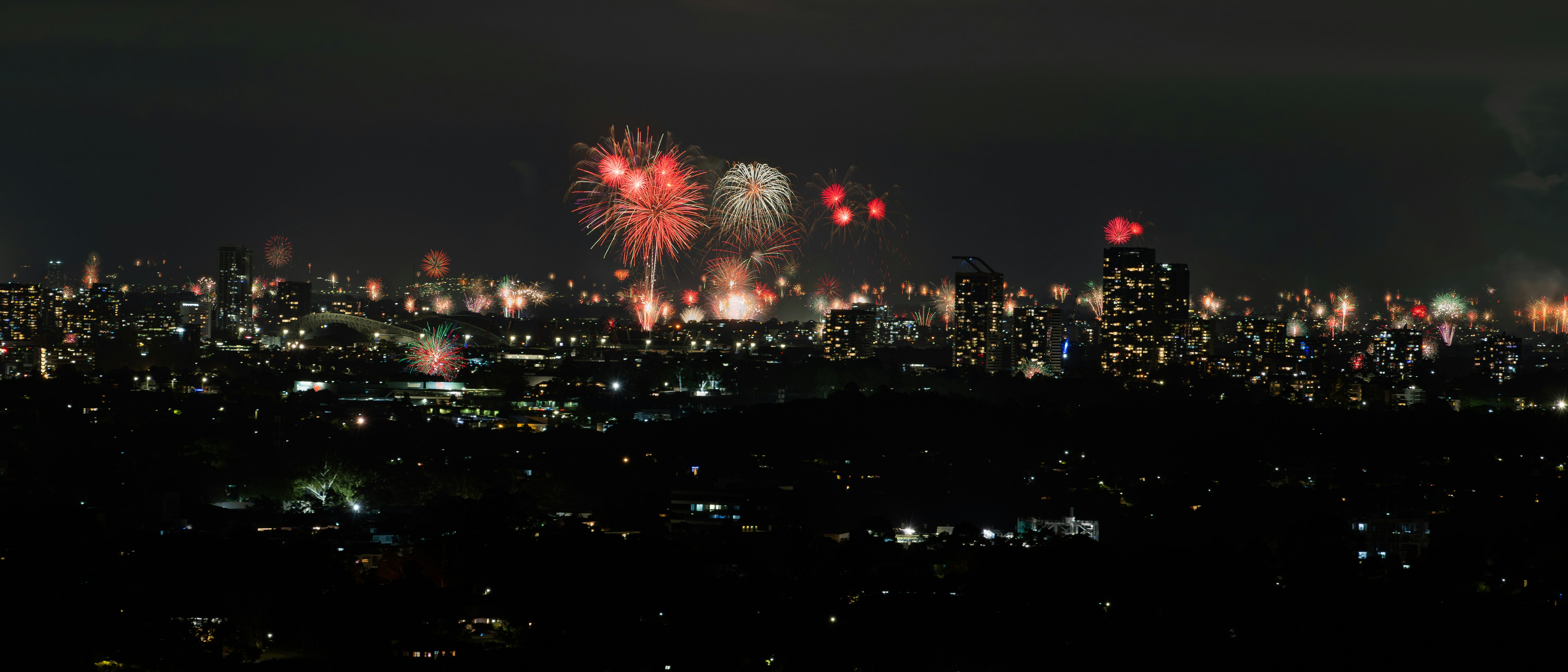 Fireworks illuminate the night sky over a city.