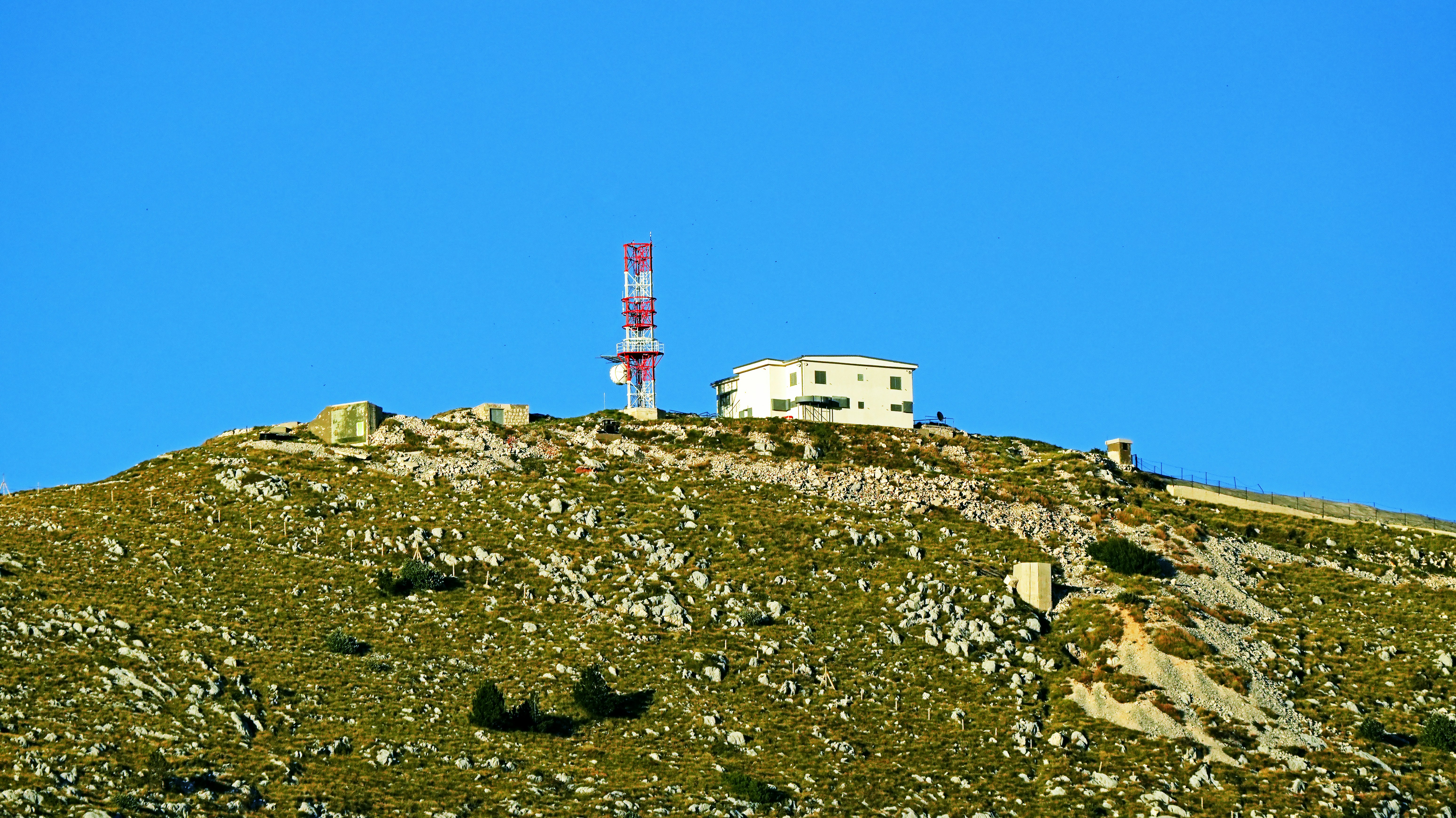 Building and communication tower atop a rocky mountain.