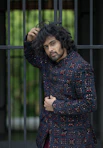 Stylish man in a dark embellished jacket by a fence