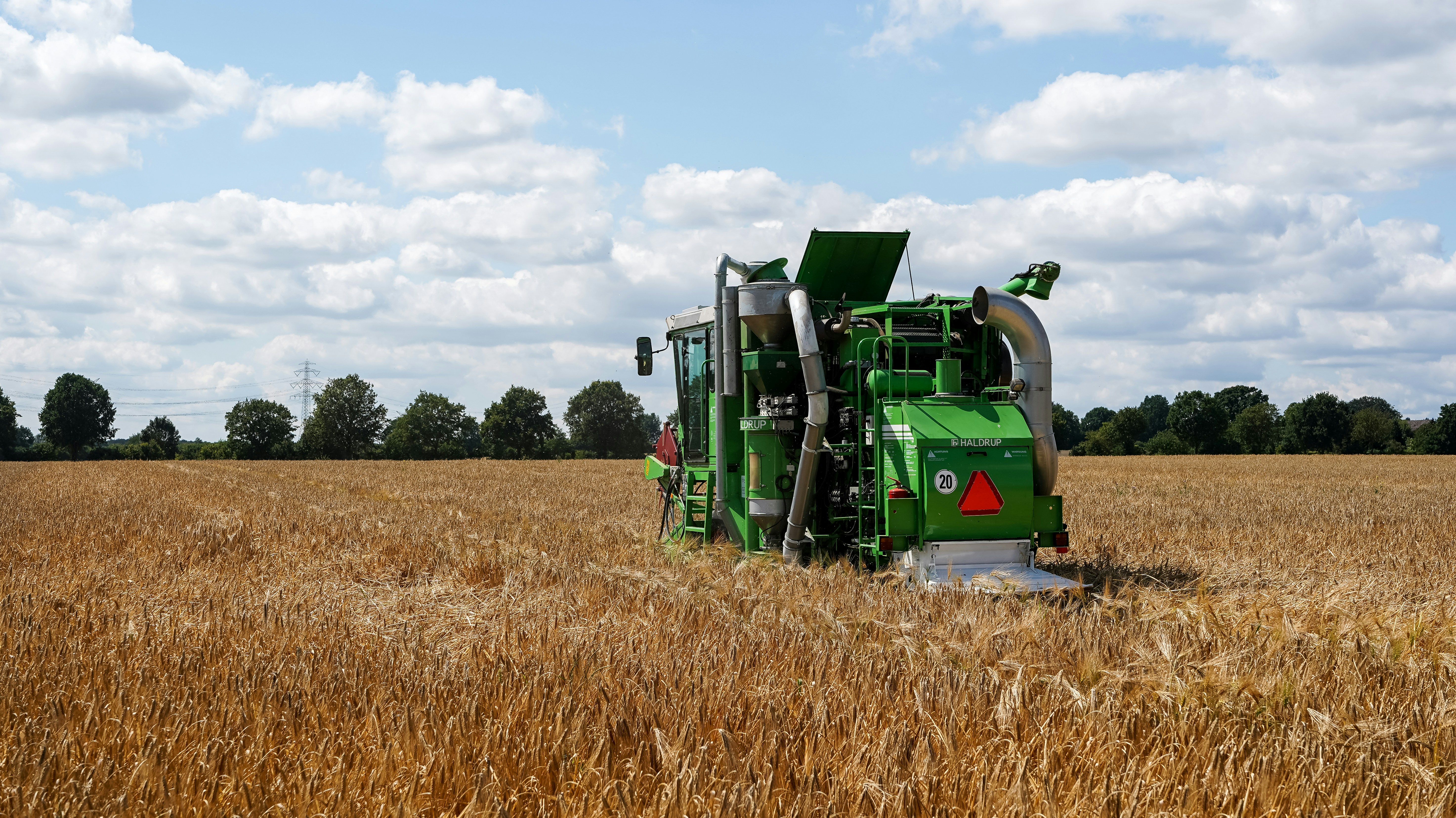 Technology A Green Agricultural Machine Harvests Golden Wheat Under Blue Sky. 4K Wallpaper #3144