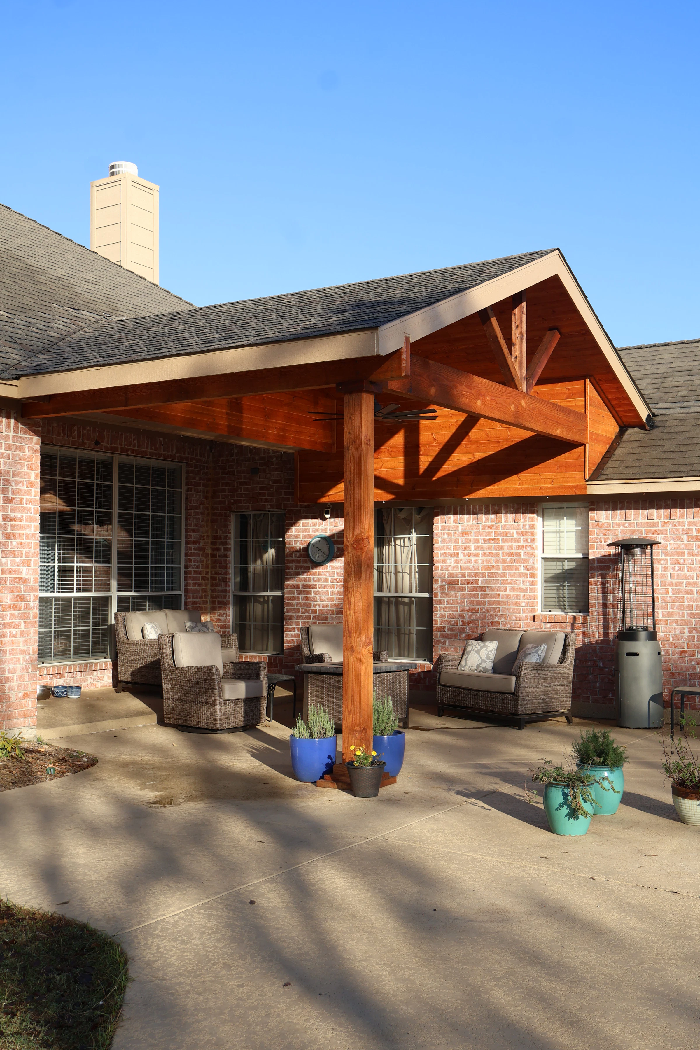 The back of a brick home with a covered wood patio and outdoor furniture