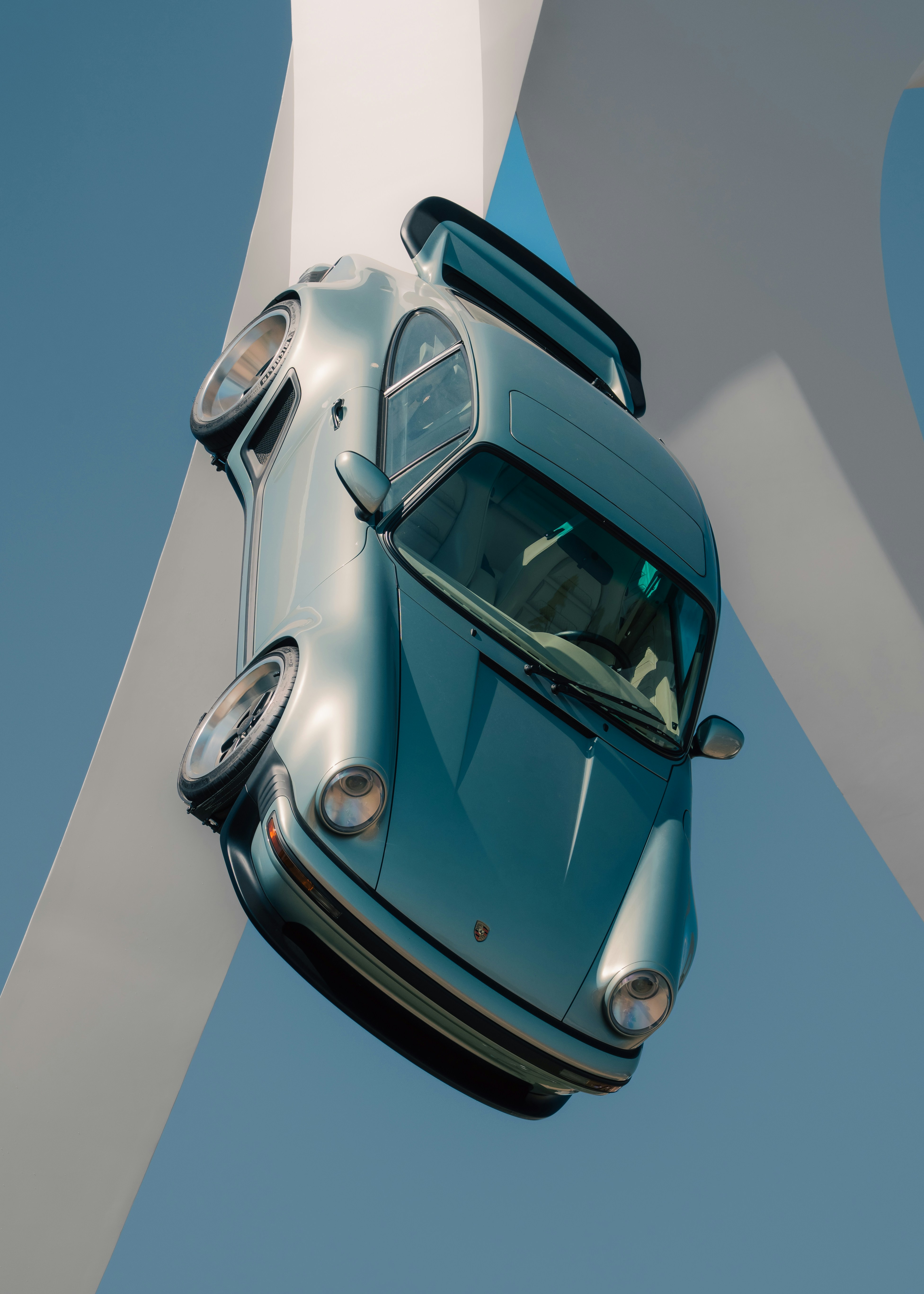 Carro esportivo vintage azul exibido verticalmente em arquitetura branca moderna.
