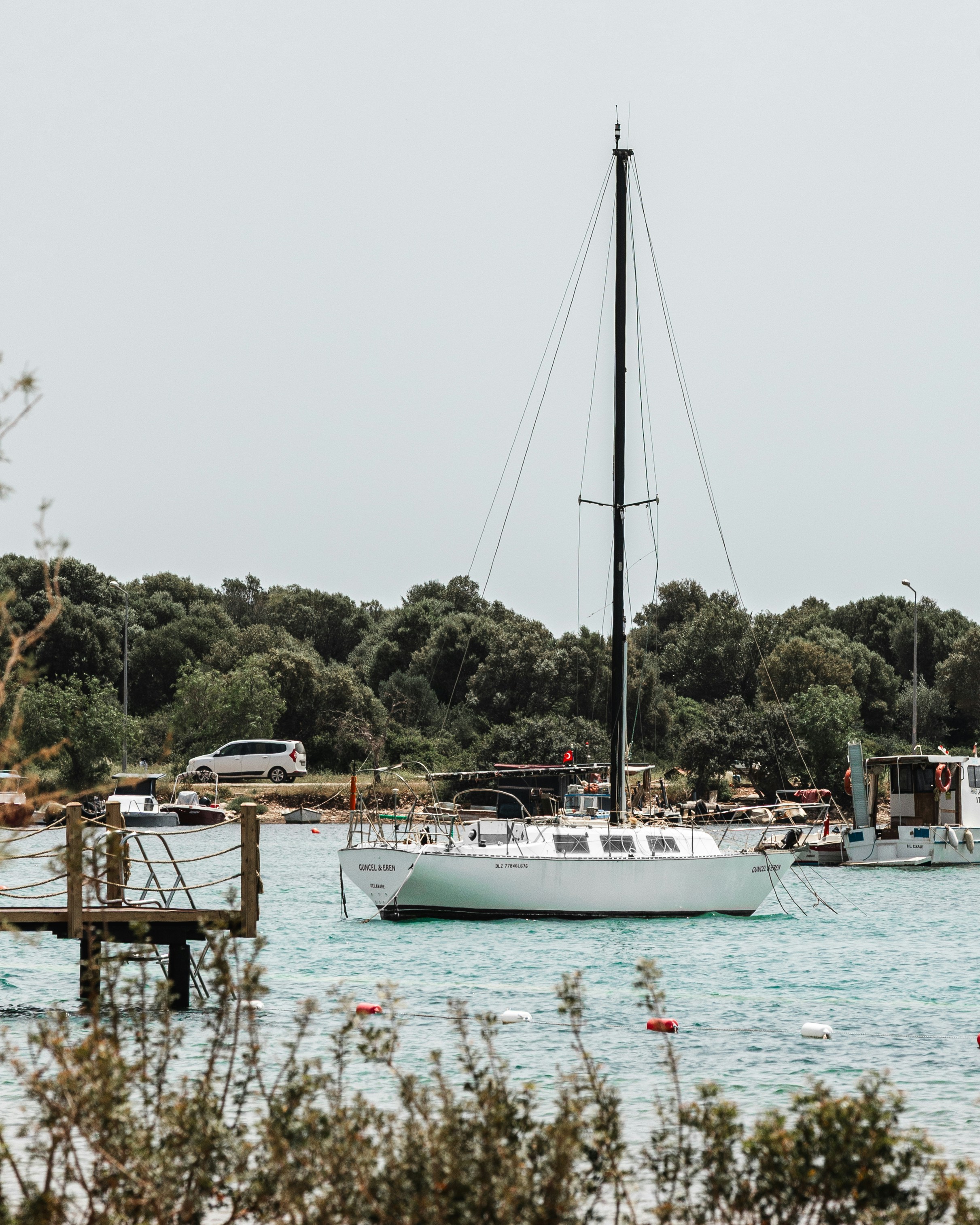 A white sailboat anchored in a bay with green trees.