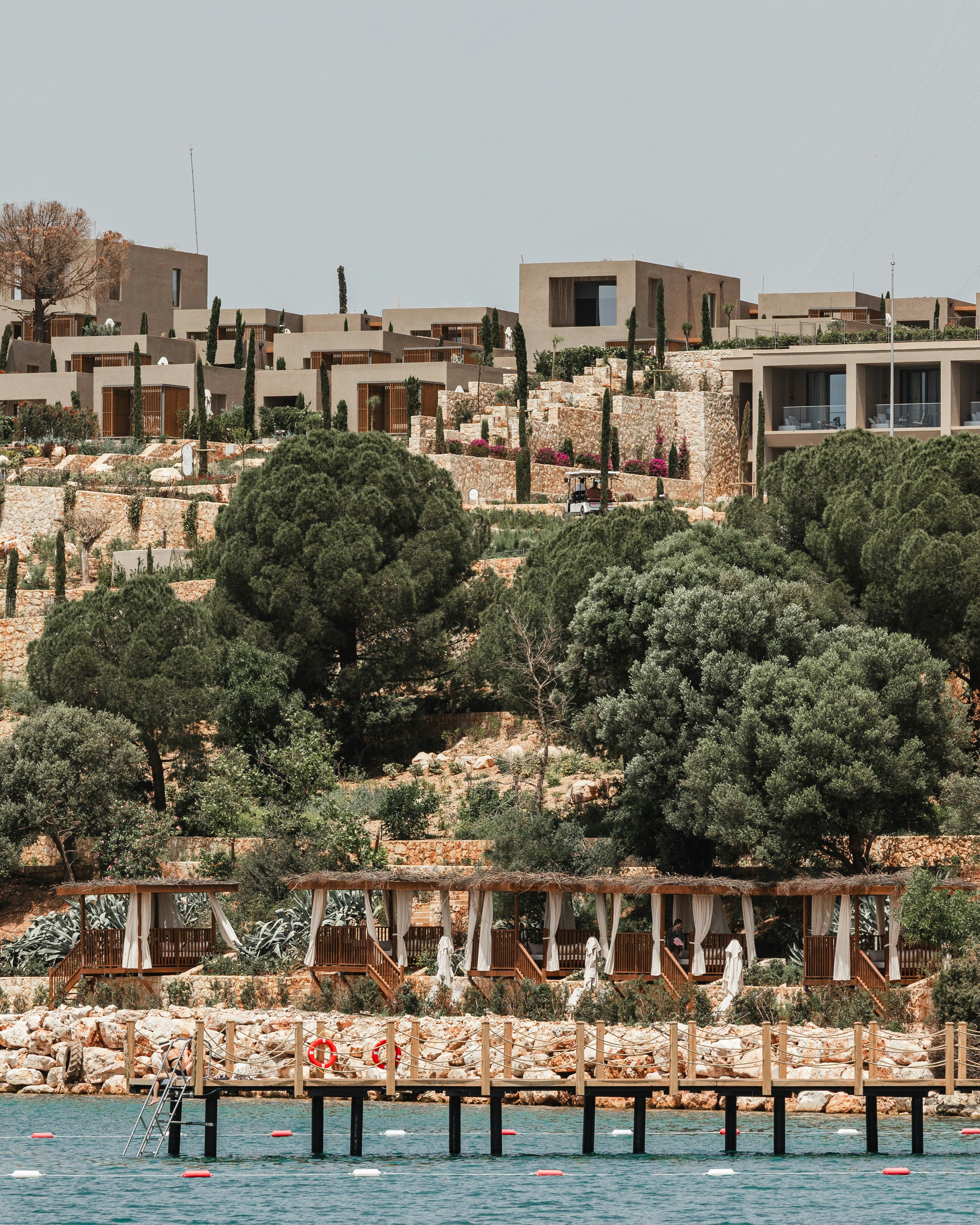 Coastal resort with pier, cabanas, and buildings on a hillside.
