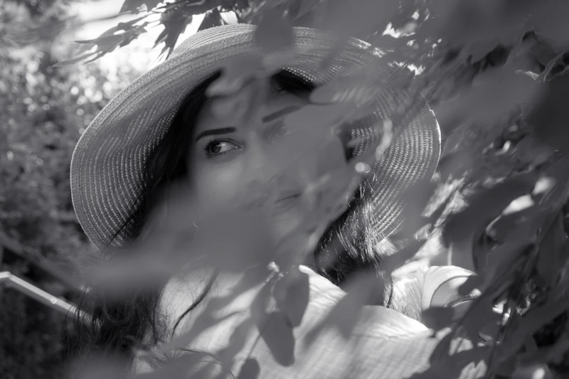 mysterious woman in a hat framed by foliage