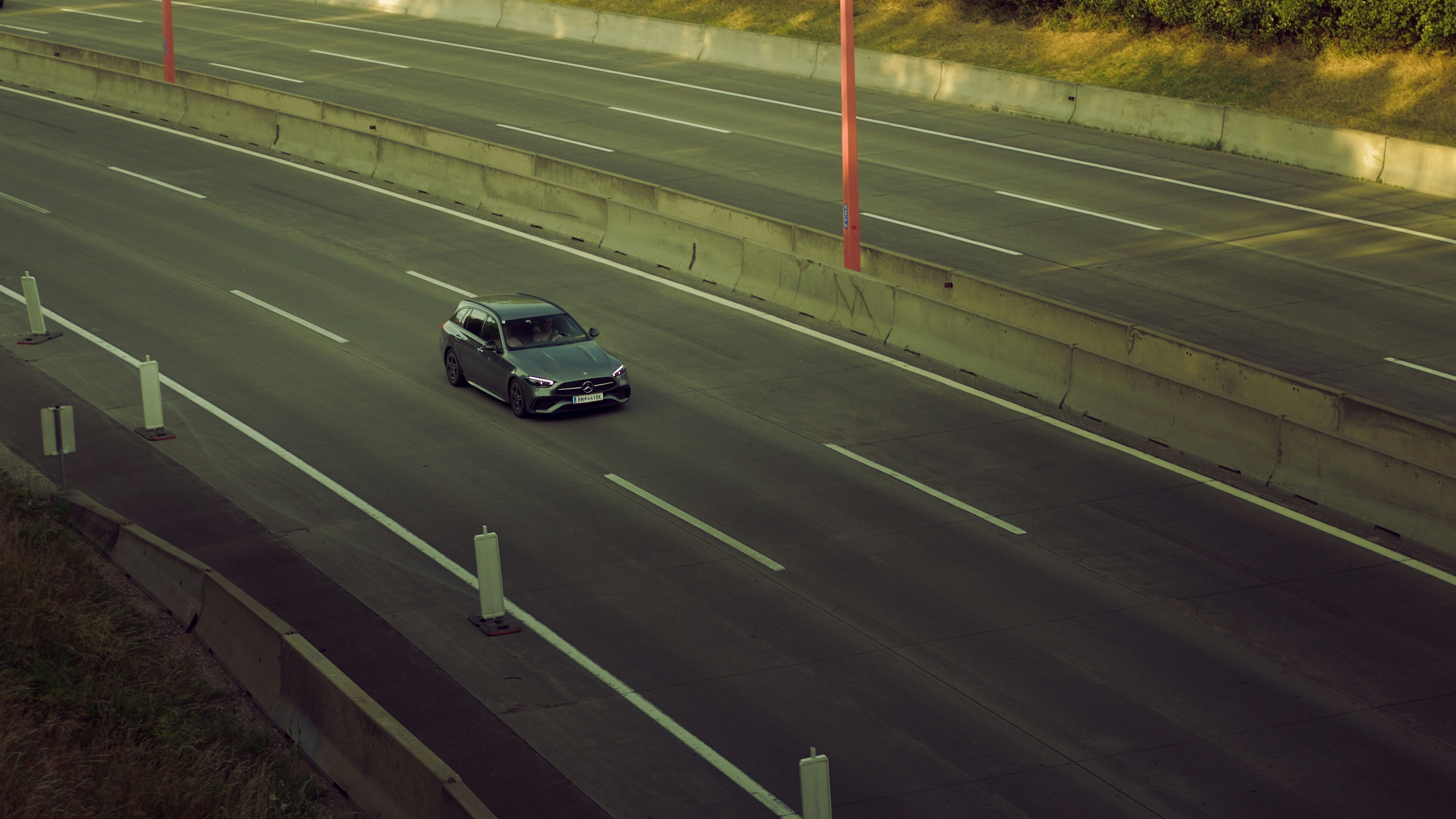 A dark car drives alone on a multi-lane highway.
