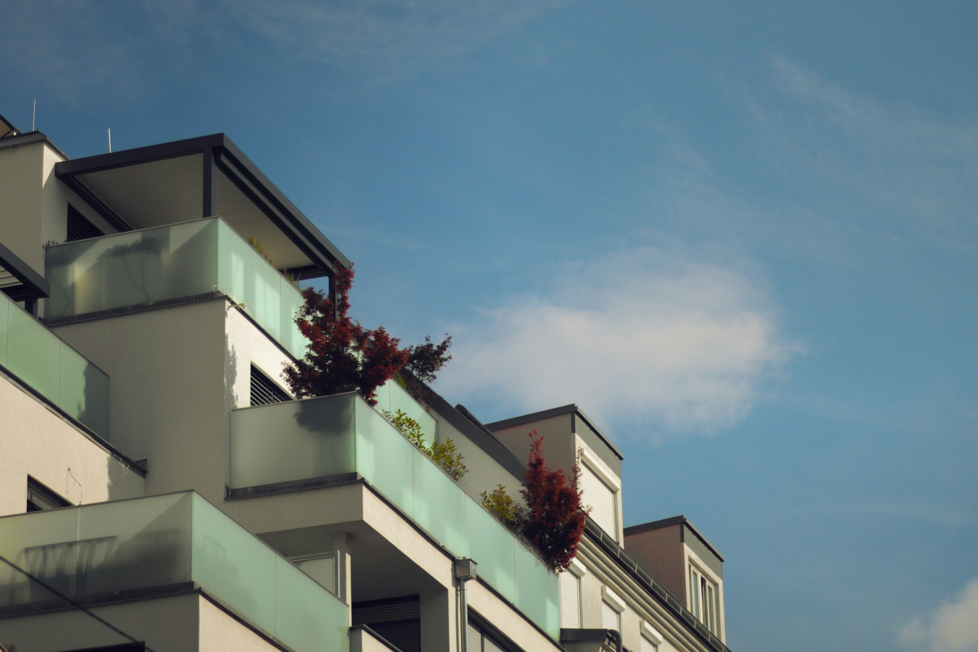 Modern building with balconies and plants against a blue sky.