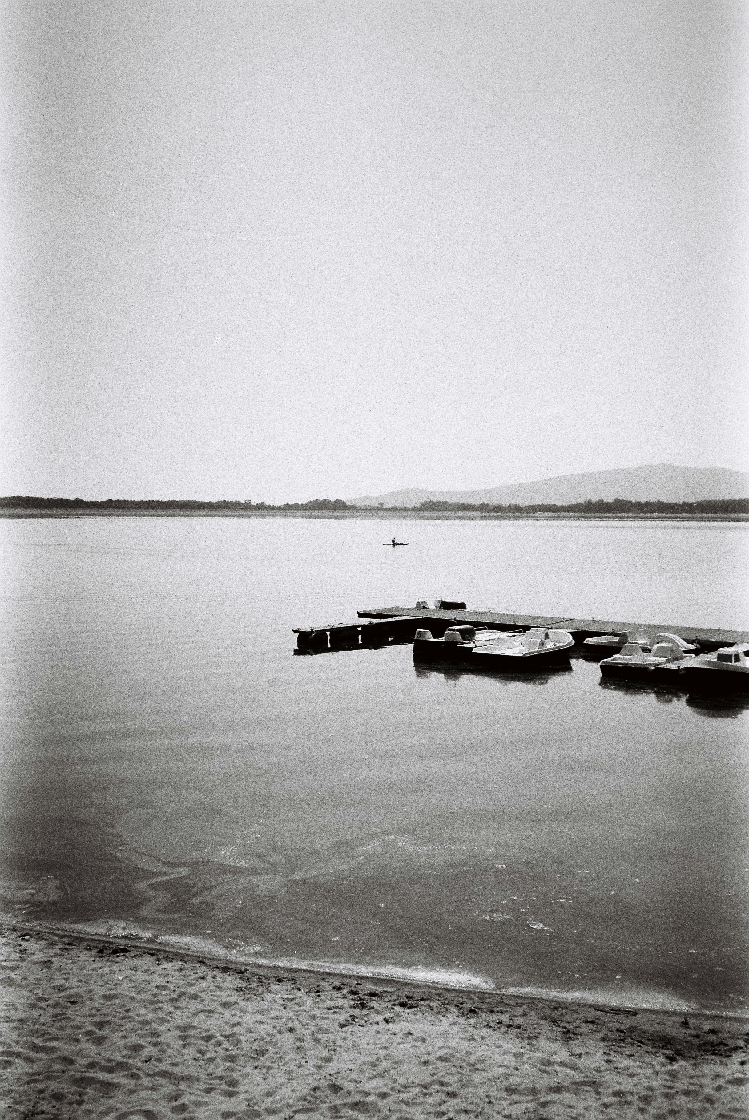 Serene lake with a dock, boats, and distant kayaker