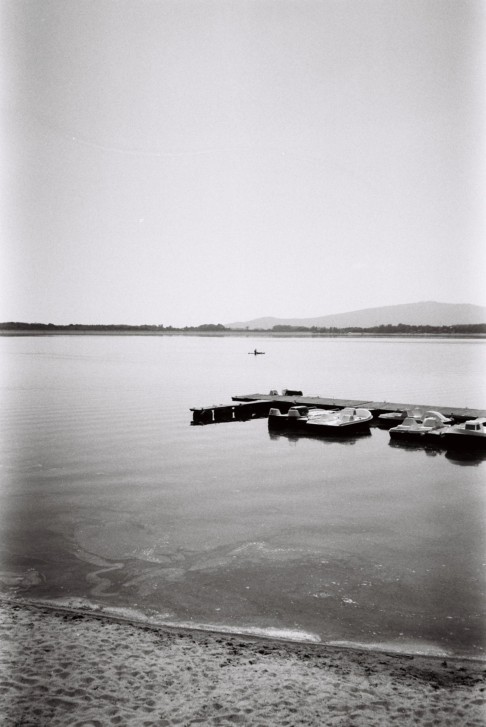 A calm Georgian Bay lake with a wooden dock, docked boats, and a distant kayaker
