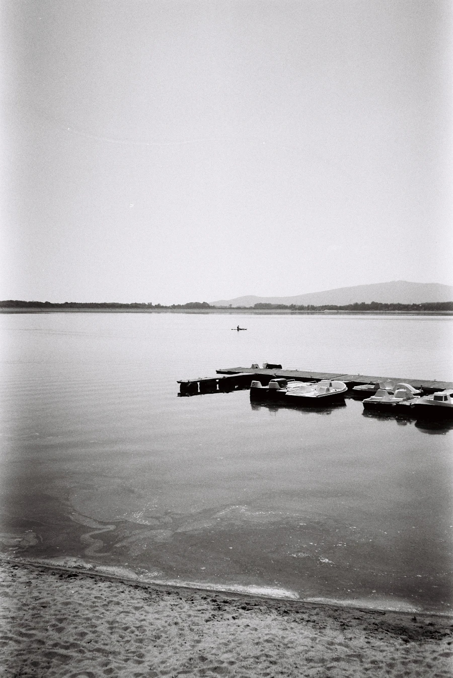 Wooden dock stretching into a calm lake with a kayaker paddling in the distance on a summer day
