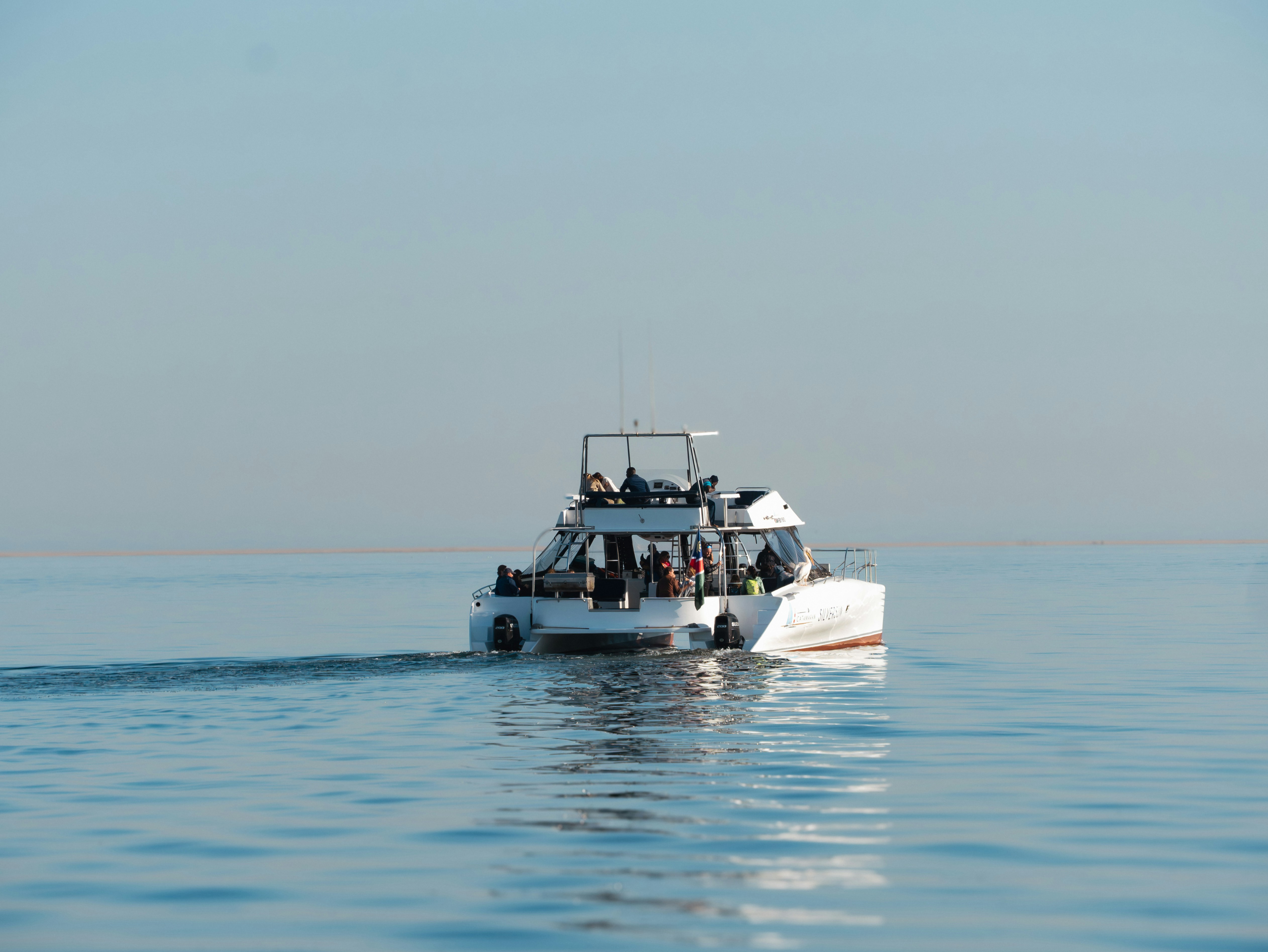 A white boat with people sails on calm blue water.