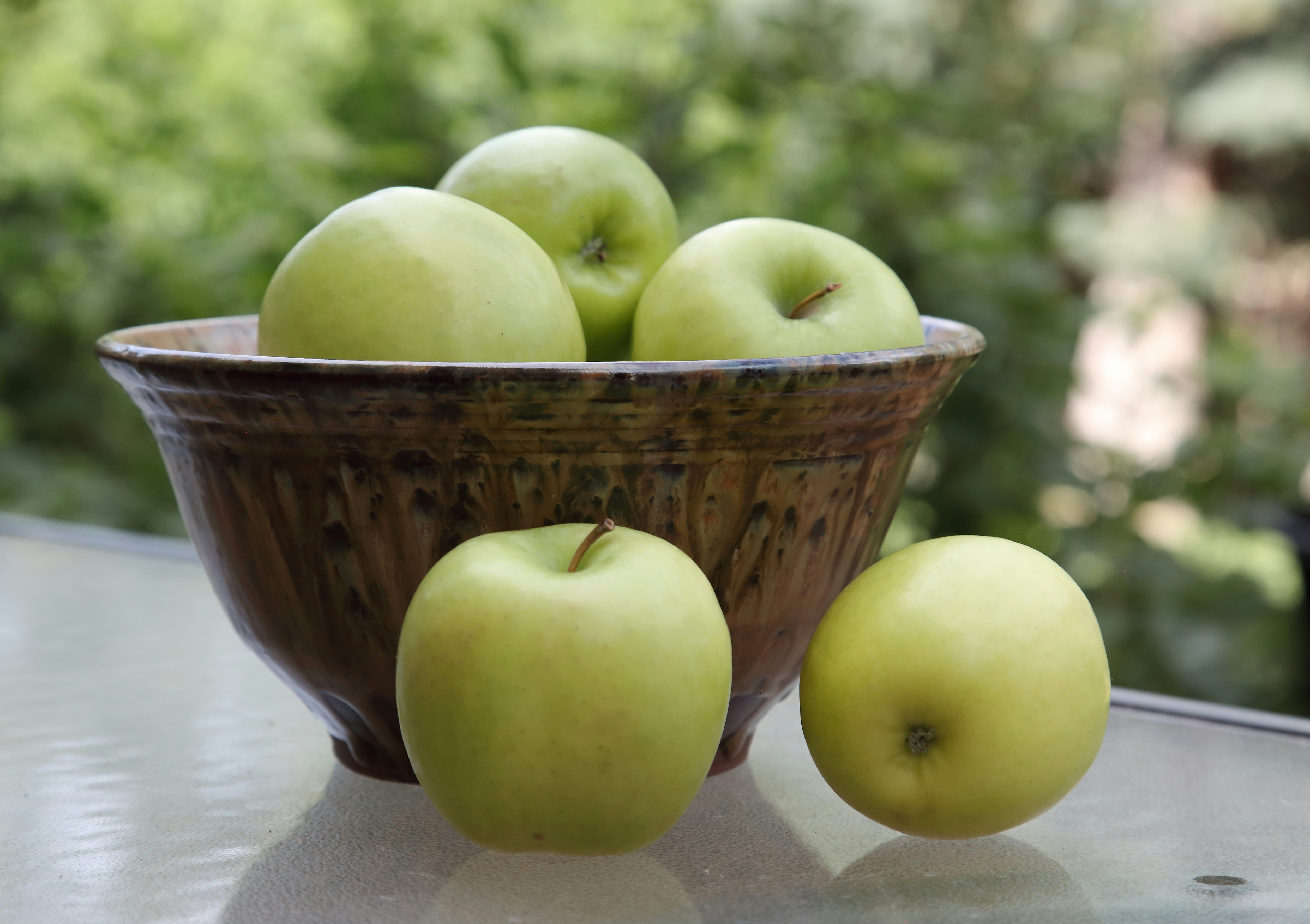 A brown bowl filled with green apples on a table