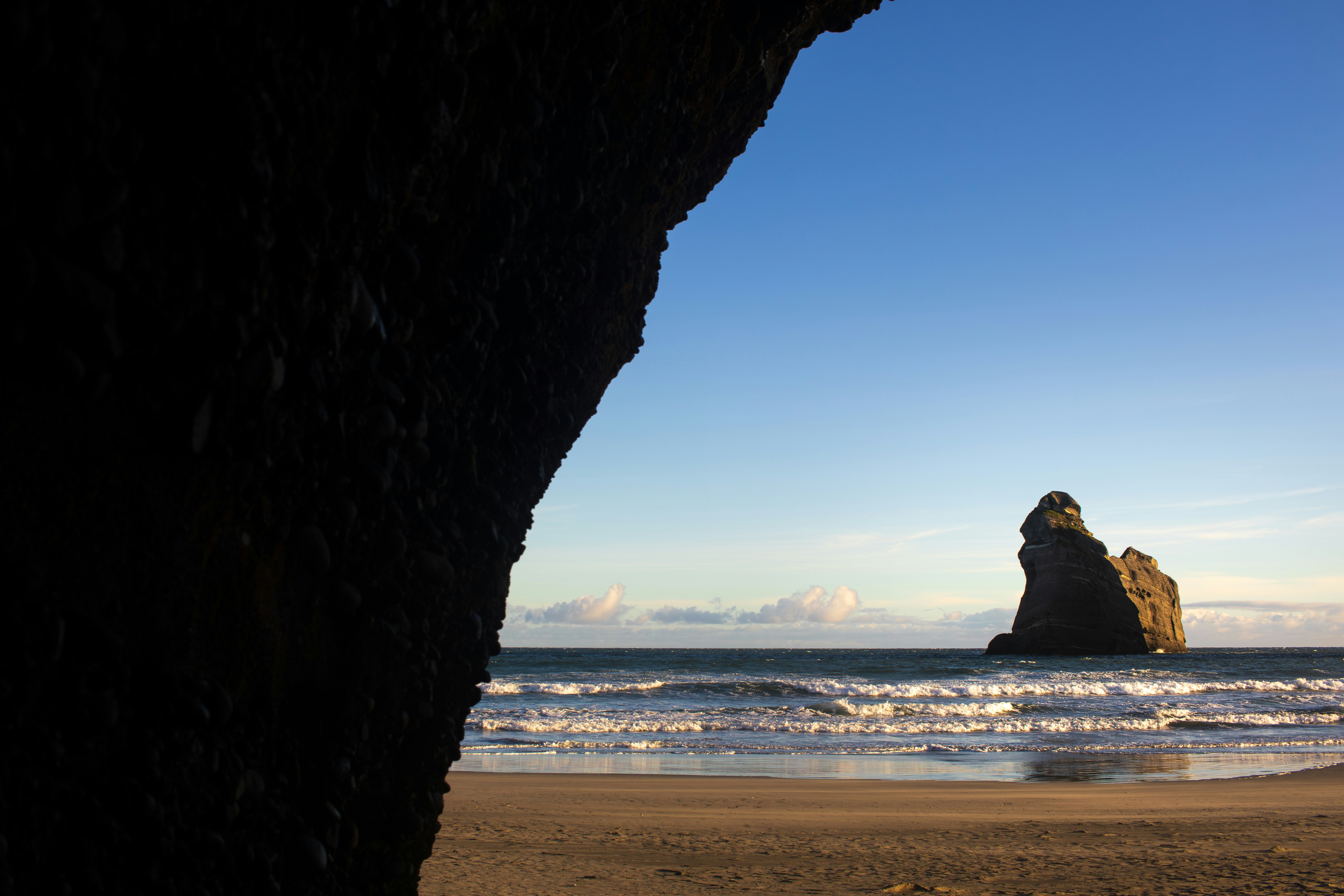 Sea stack in ocean with beach, framed by dark rock