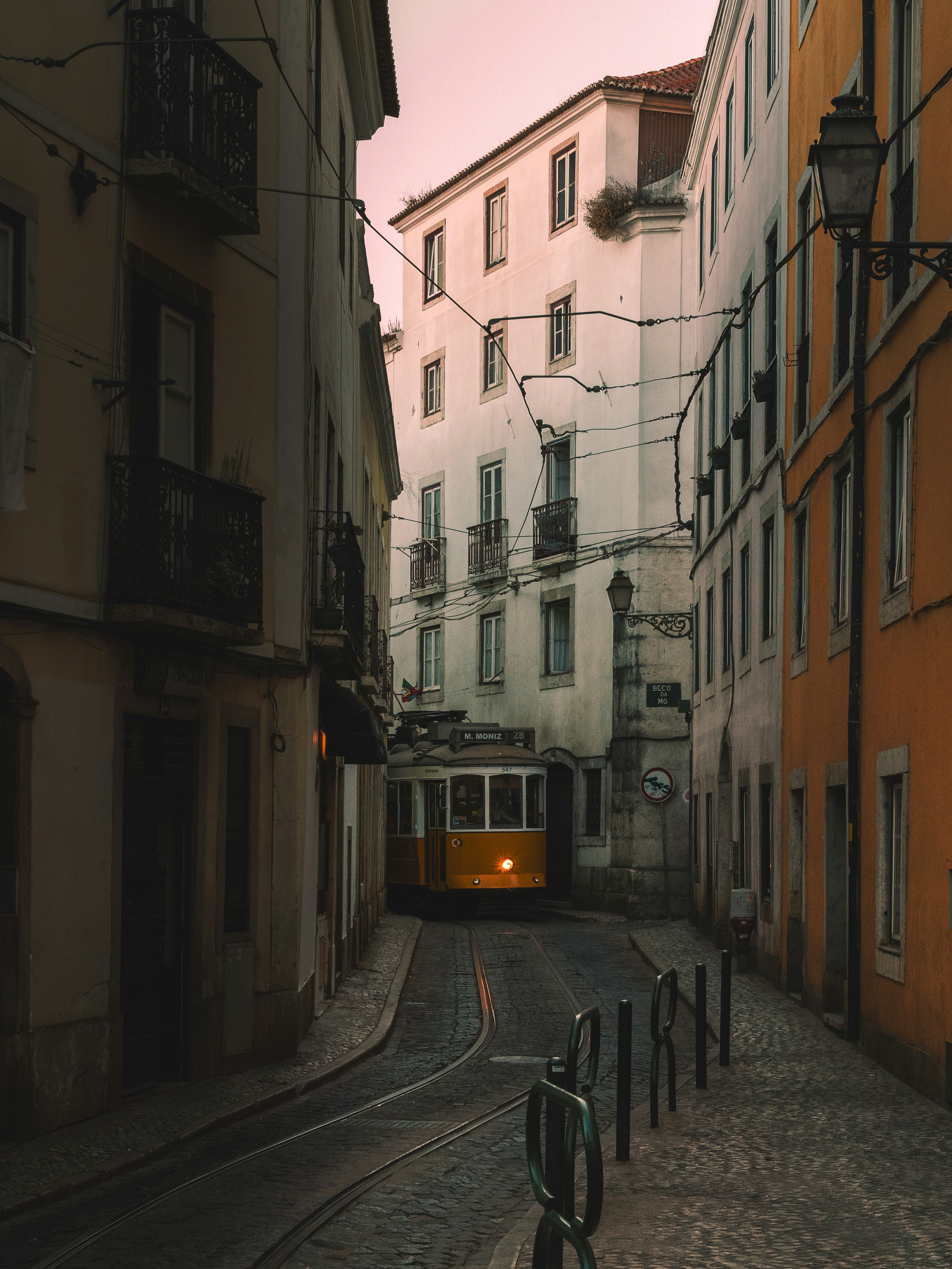 A yellow tram on a narrow cobblestone street at dusk.