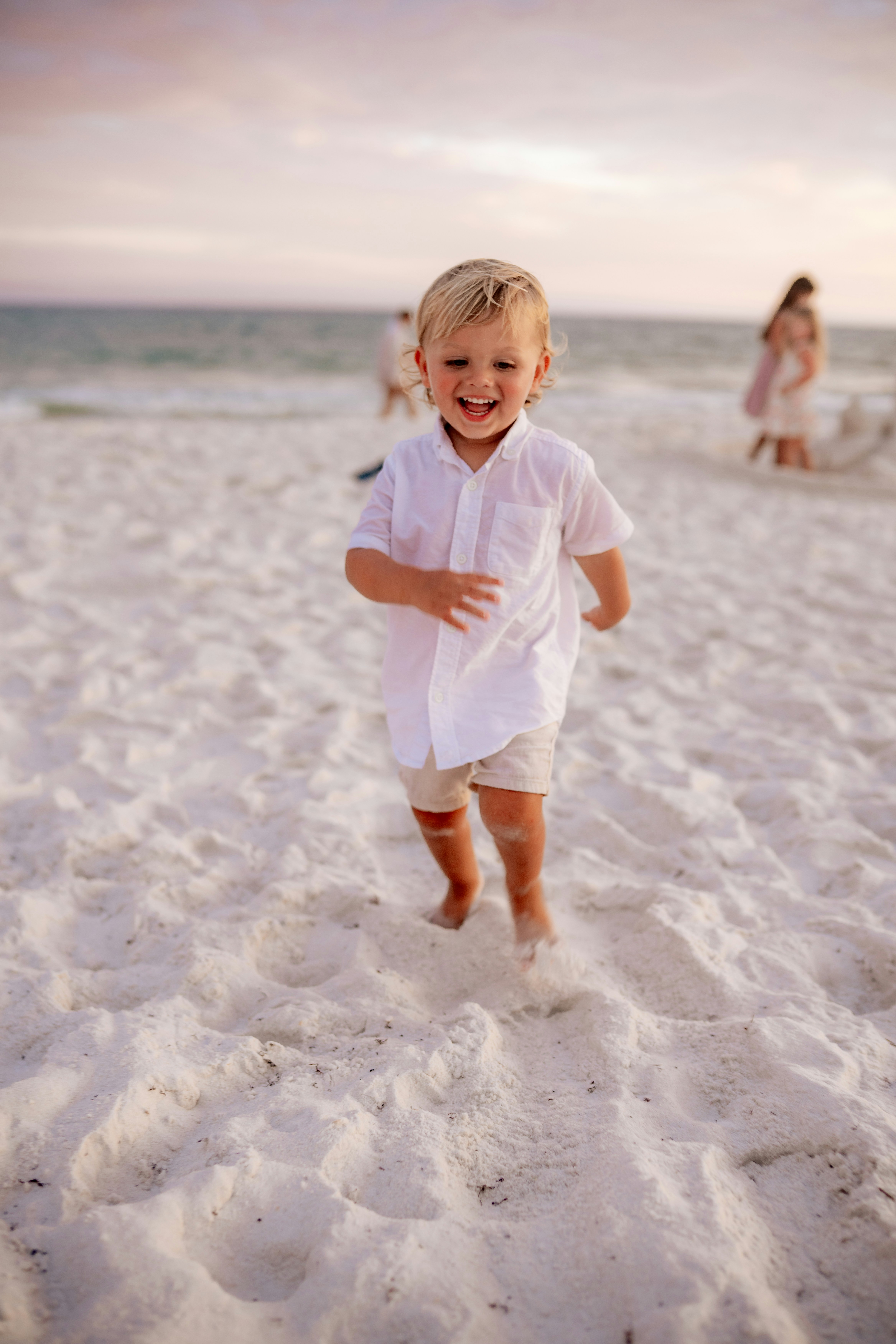 Smiling boy runs barefoot on white sand beach.