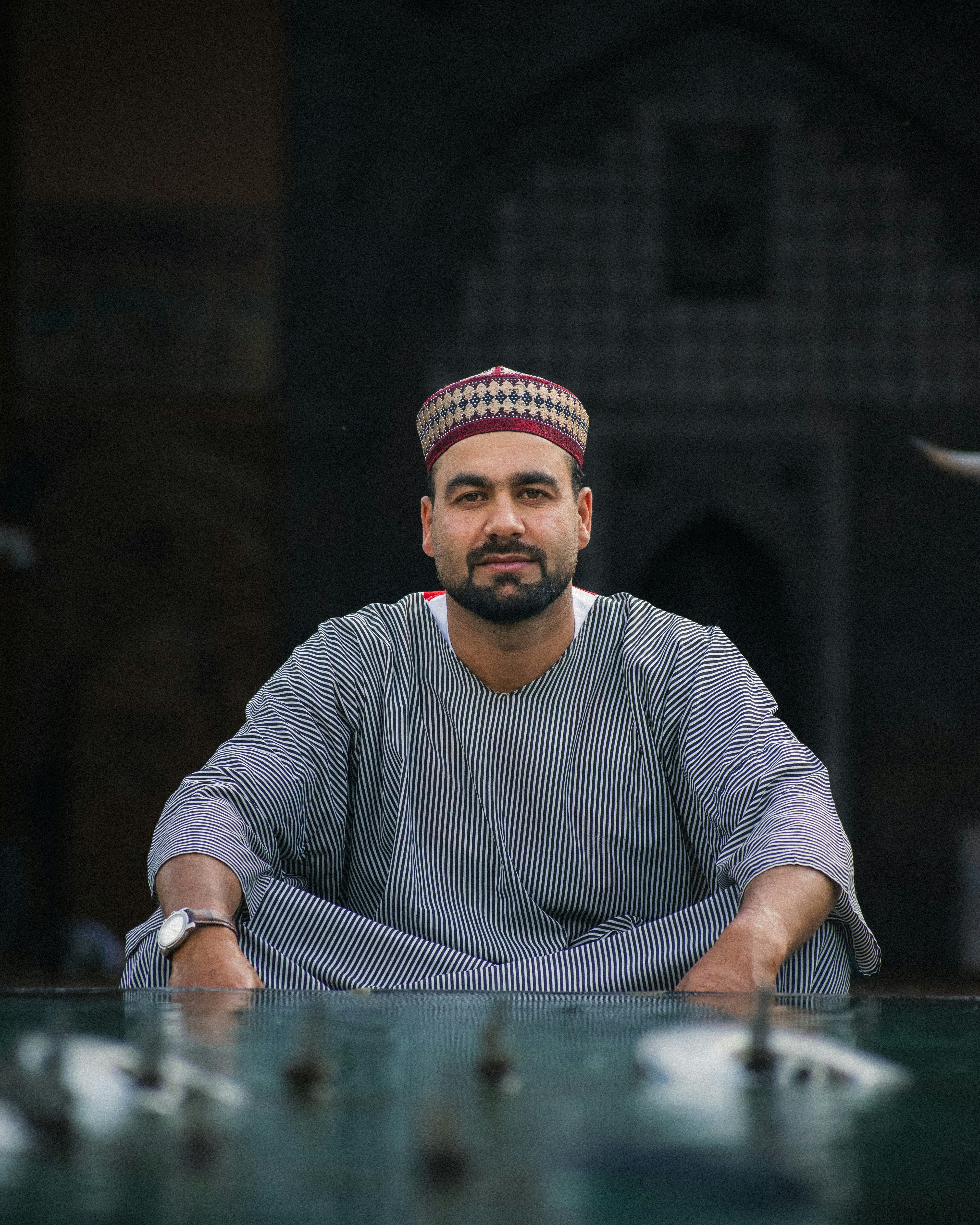 Man in traditional clothing sits by a reflective water surface.
