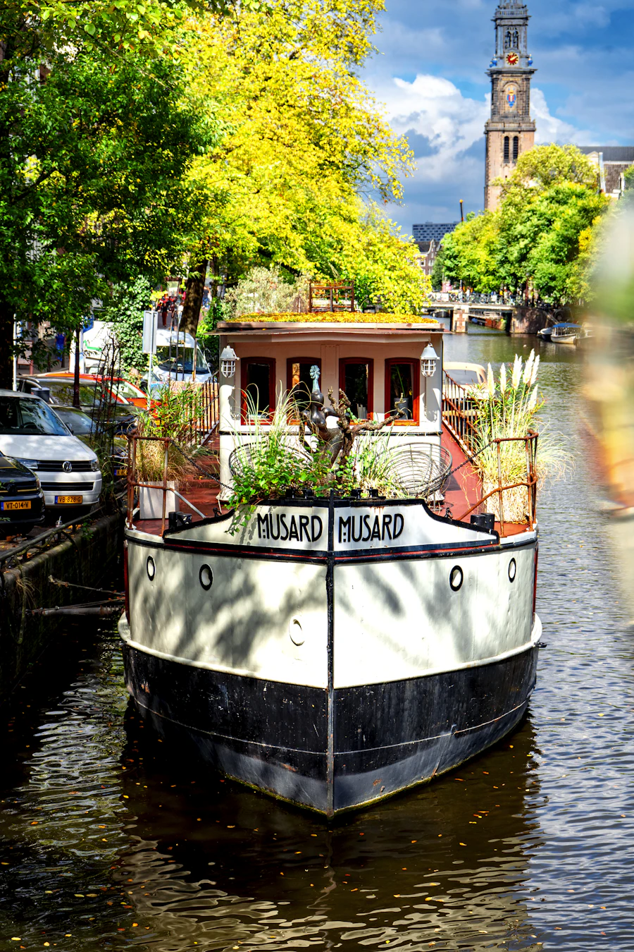 Blossom, a houseboat with flower boxes along its roof moored on a sunny canal