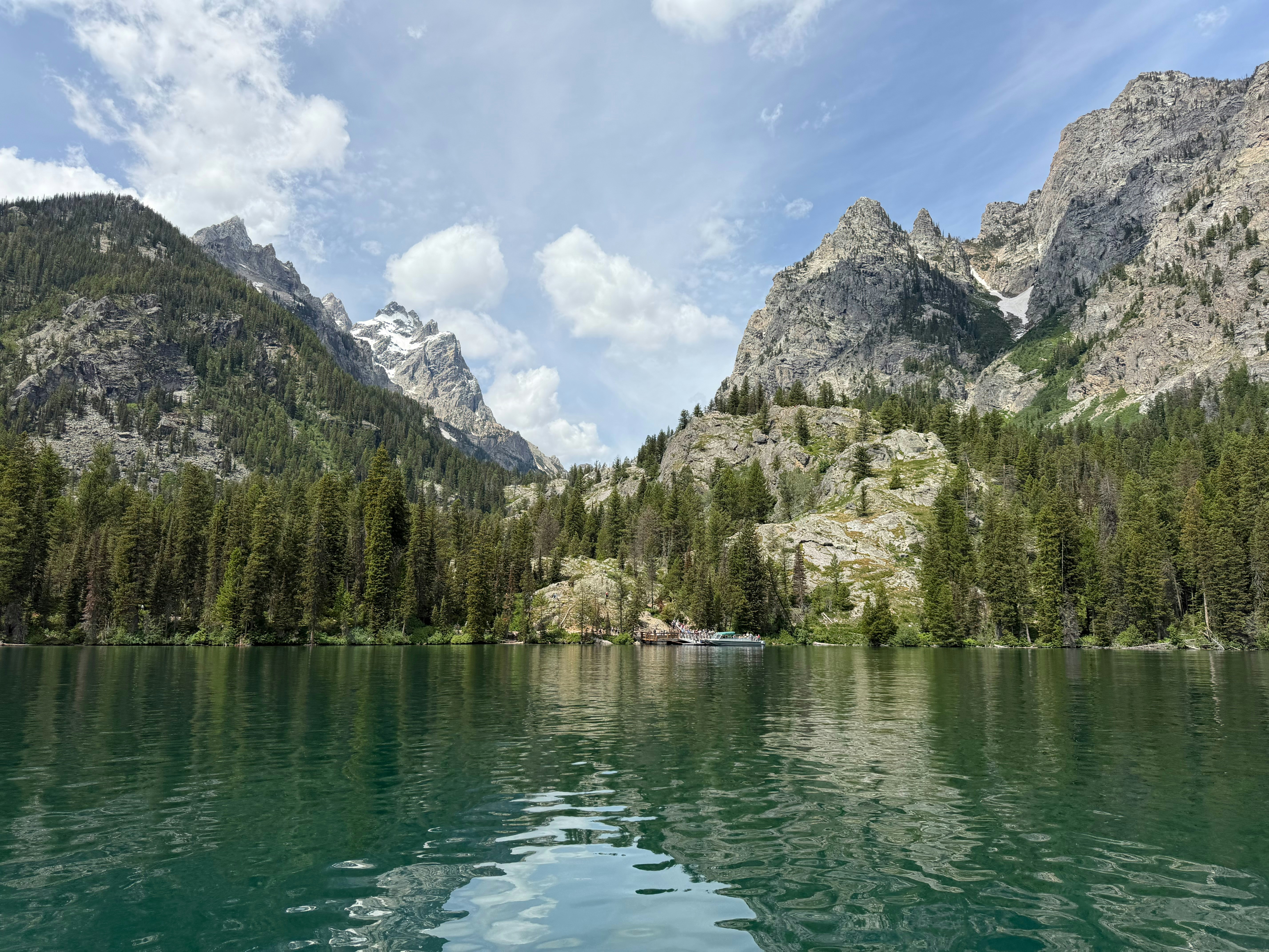 Danau yang tenang dengan pegunungan dan hutan di bawah langit biru.