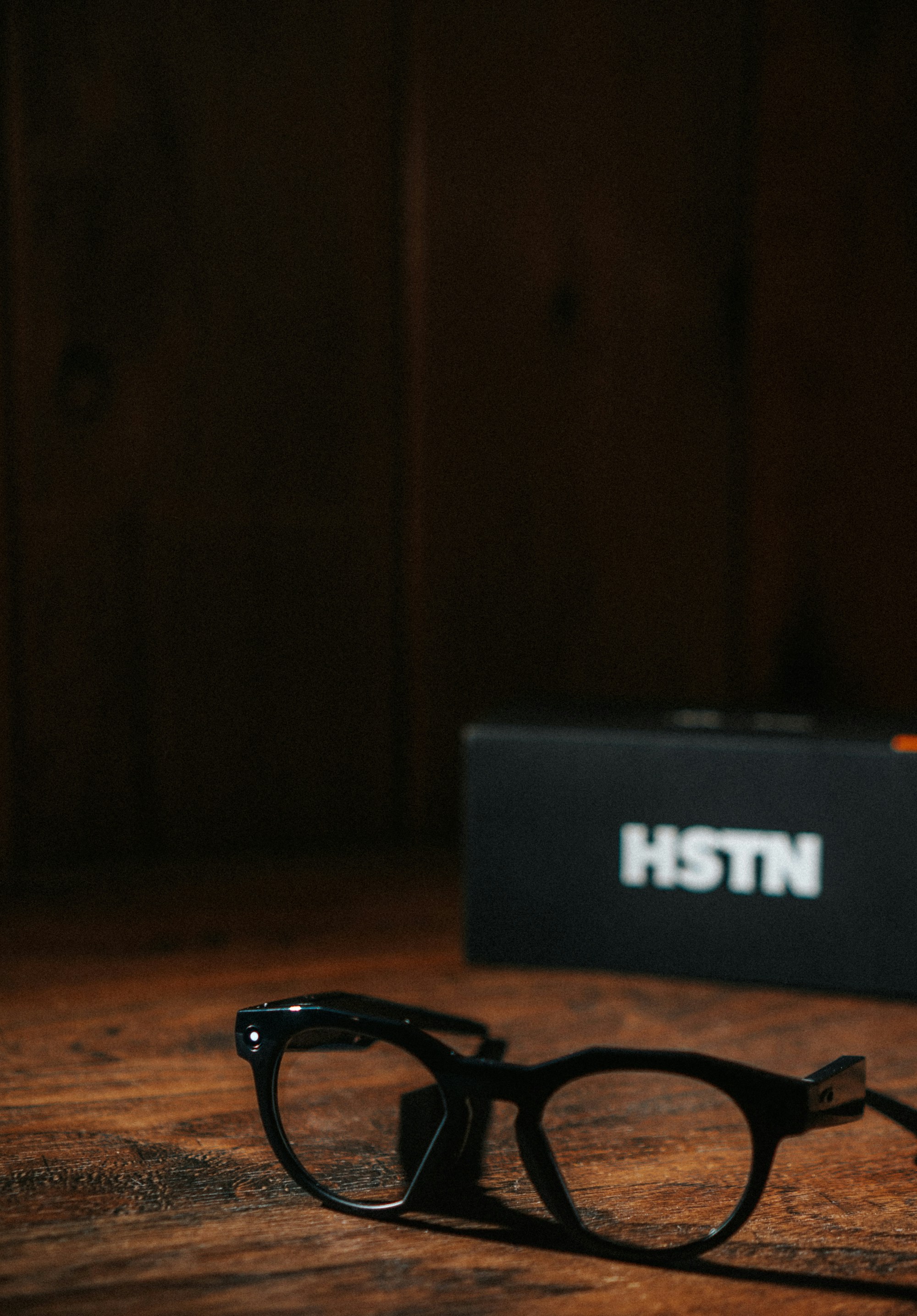 Black glasses and an hstn box on a wooden table.