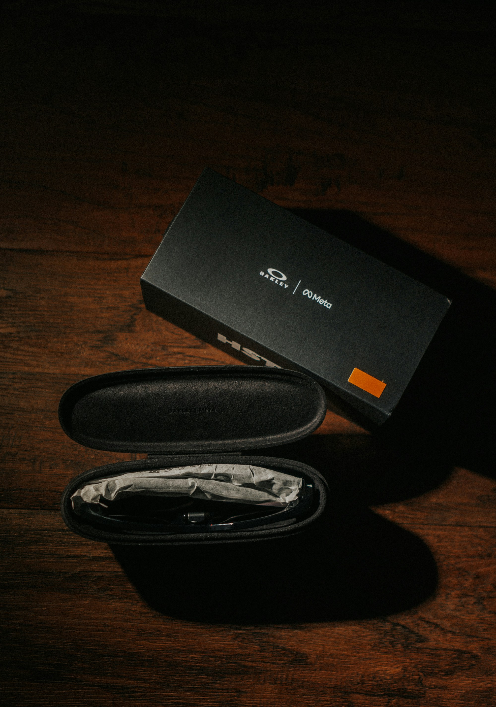 Oakley sunglasses box and open case on dark wood.