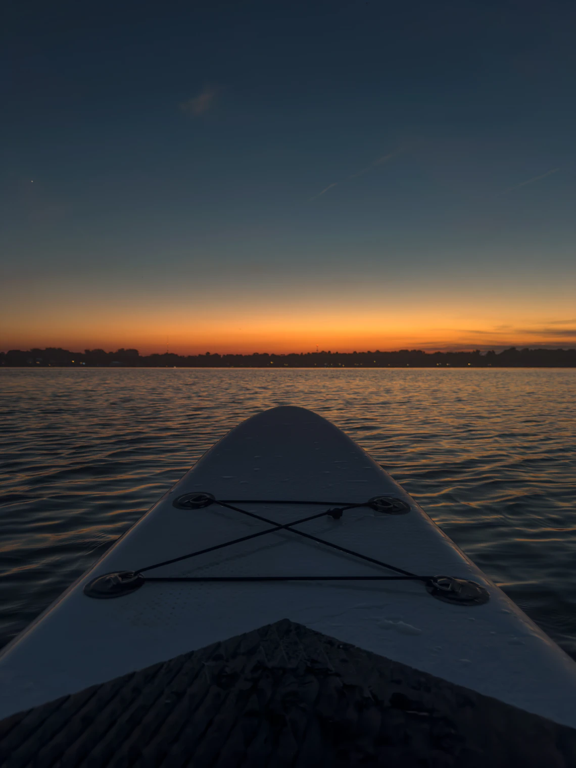 Paddleboarder crossing peaceful water beneath a colorful evening sky