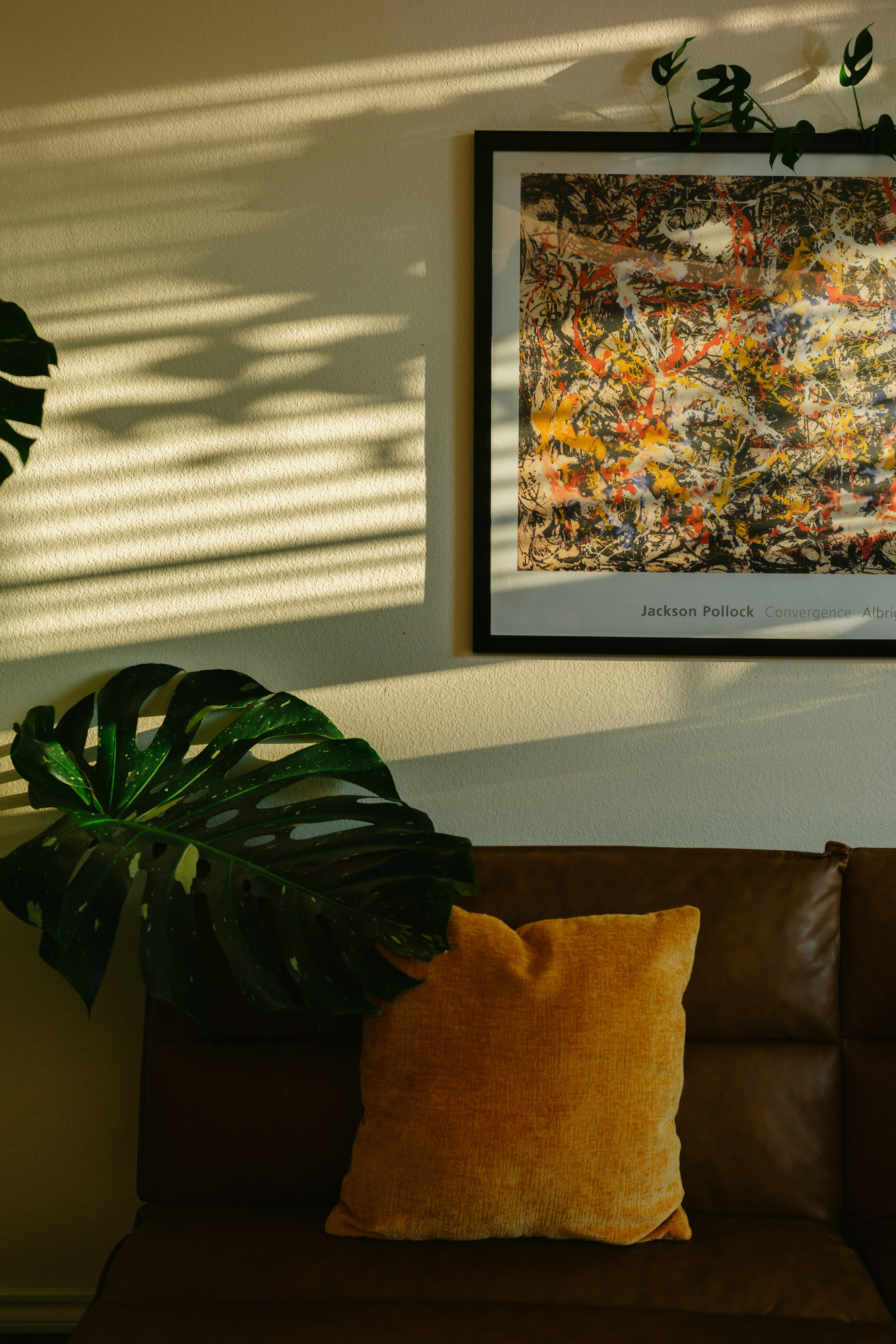 Sunlight on brown couch, monstera plant, and abstract art