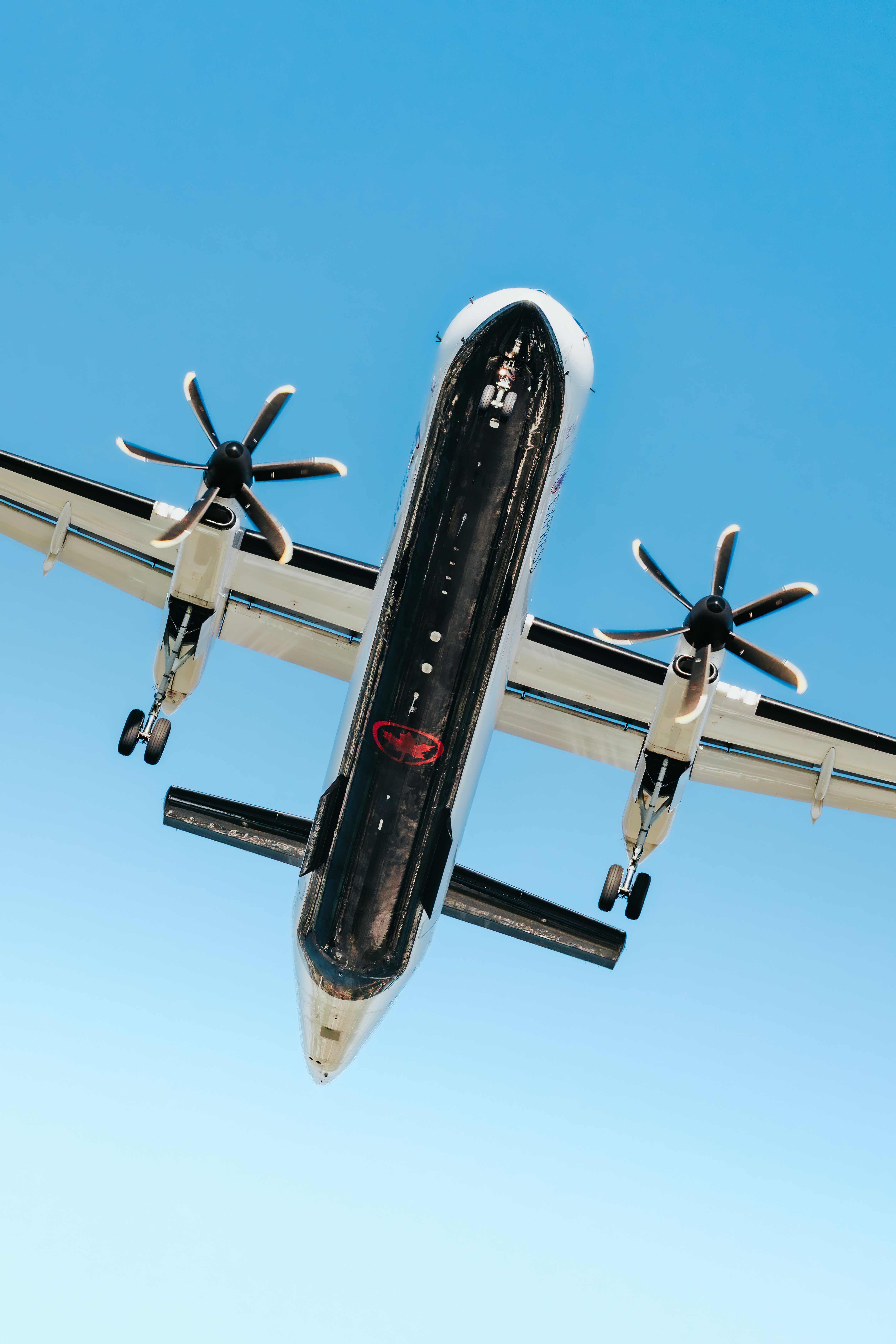 A turboprop airplane flying overhead against a clear blue sky.