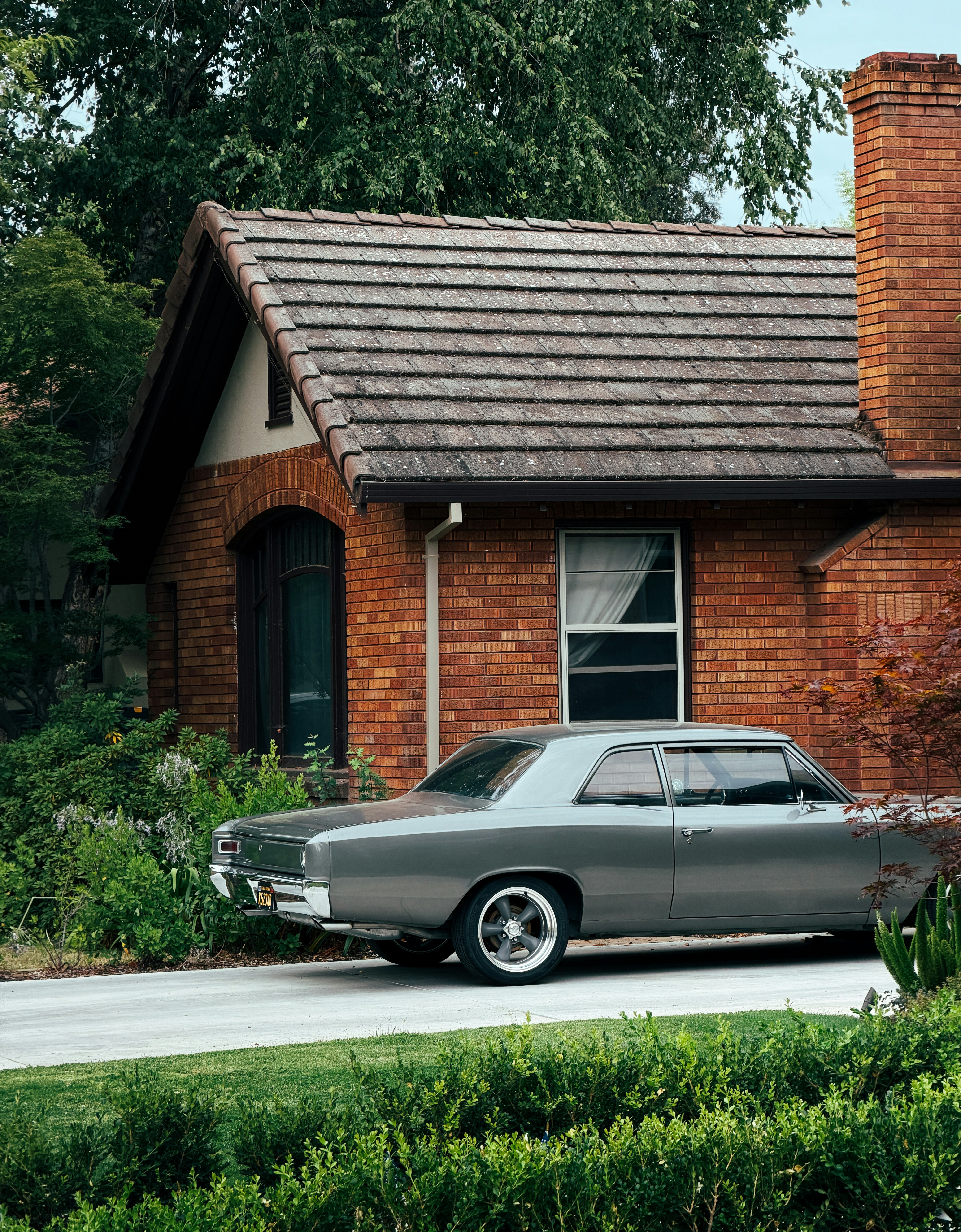 Vintage grey car parked beside a brick house.