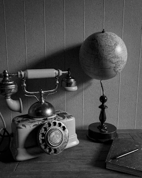 Antique rotary phone, globe, and book in monochrome.