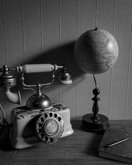 Antique rotary phone, globe, and book in monochrome.